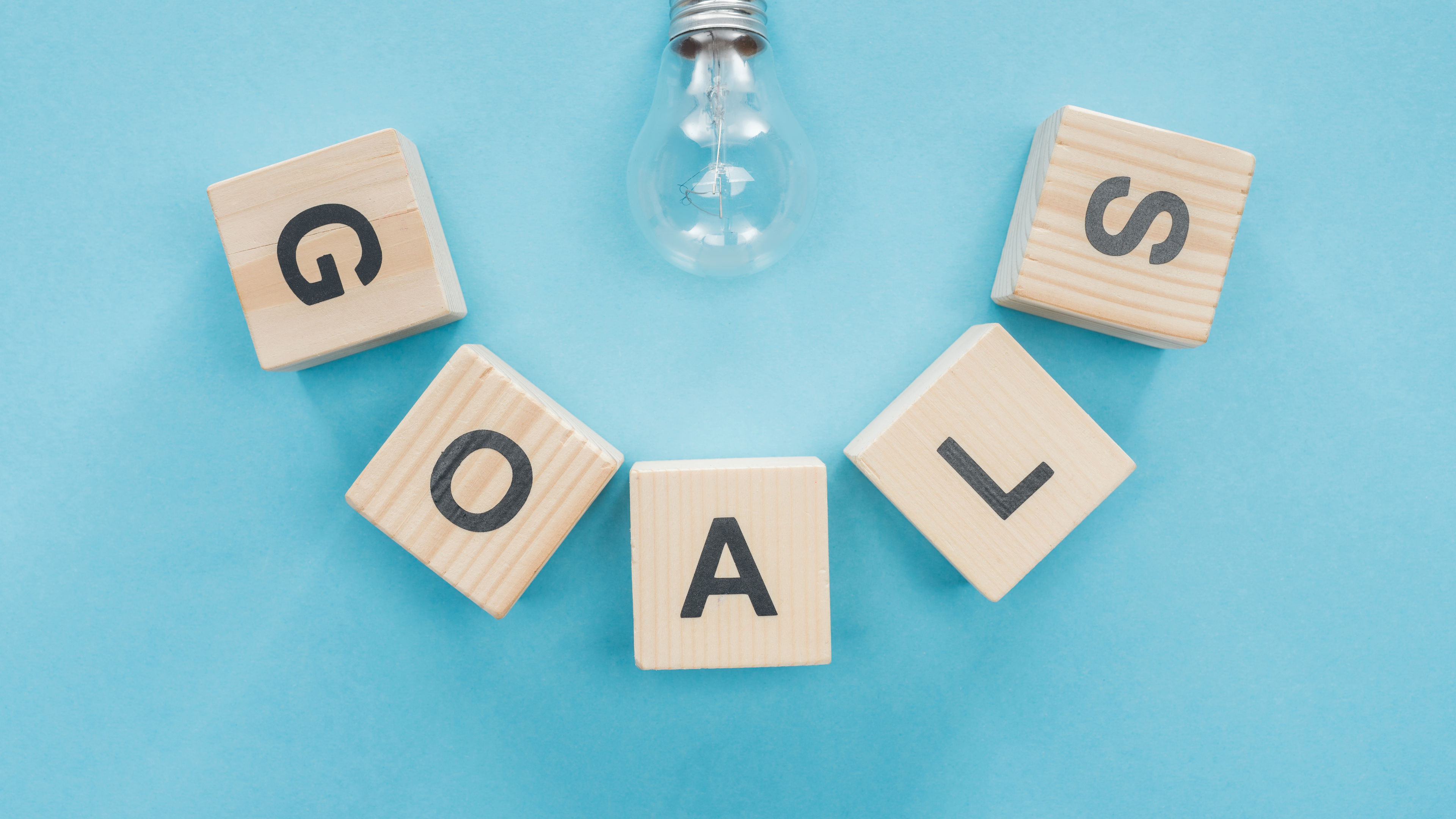 top view of light bulb over 'goals' word made of wooden blocks on blue background, goal setting 
