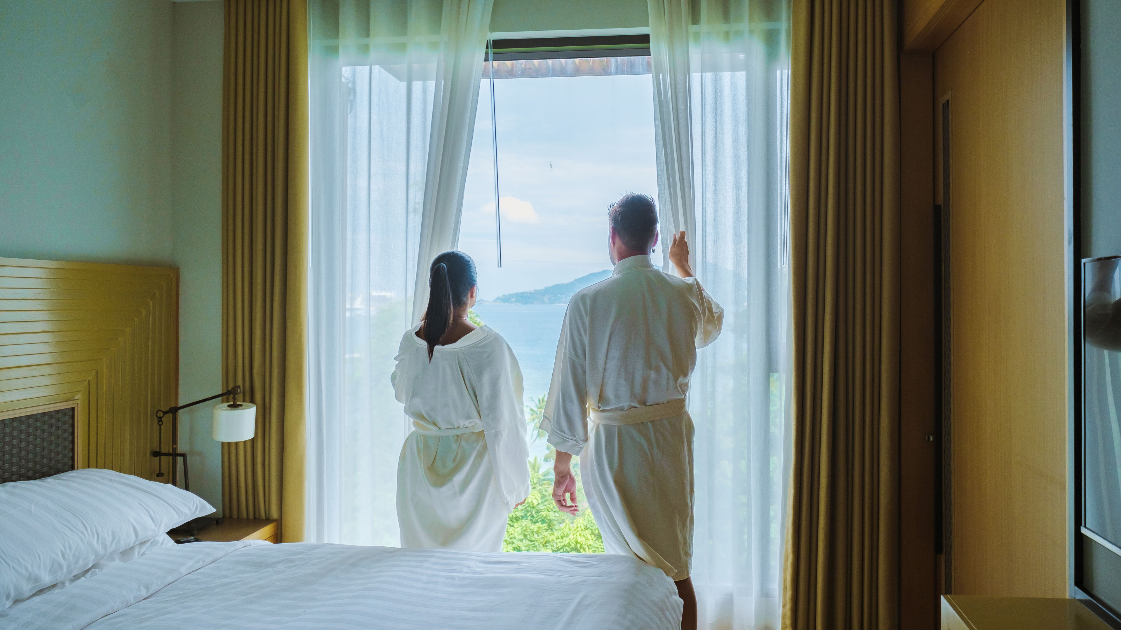 Couple holding the curtain and looking through the window