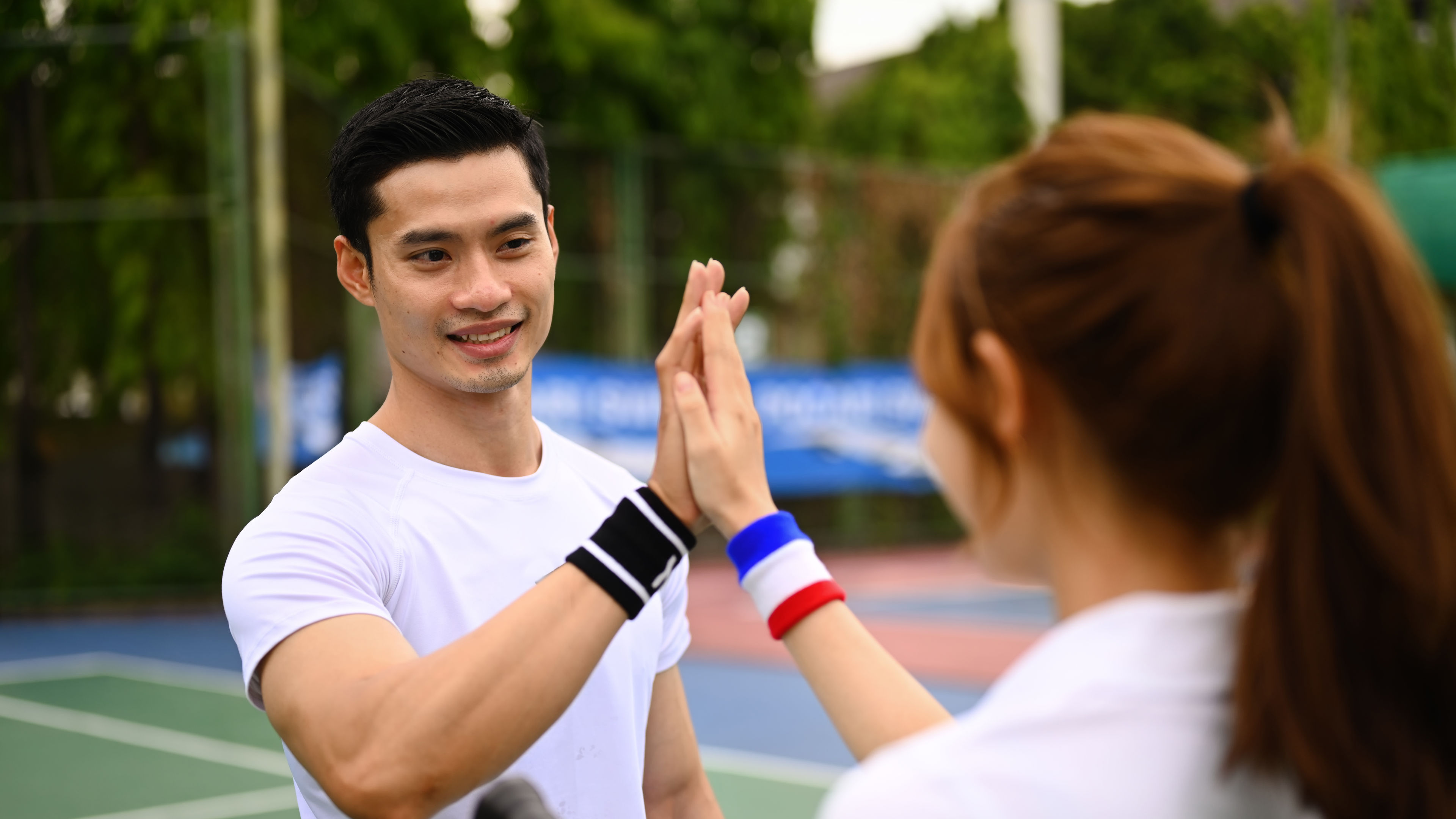Fitness sport tennis couple giving each other a high five while playing tennis together on a court. 