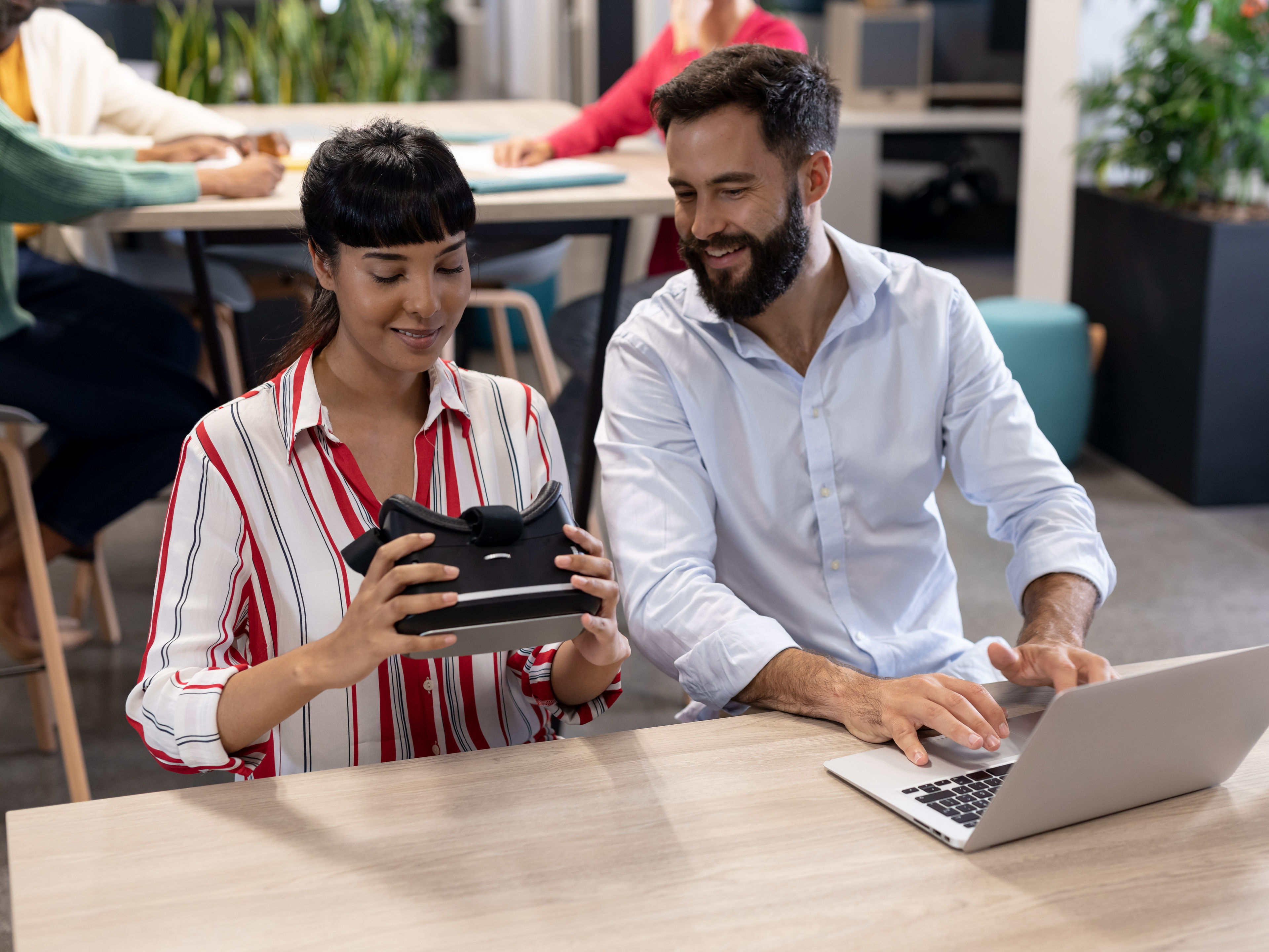Smiling biracial business colleagues discussing over vr simulator with laptop during meeting.    