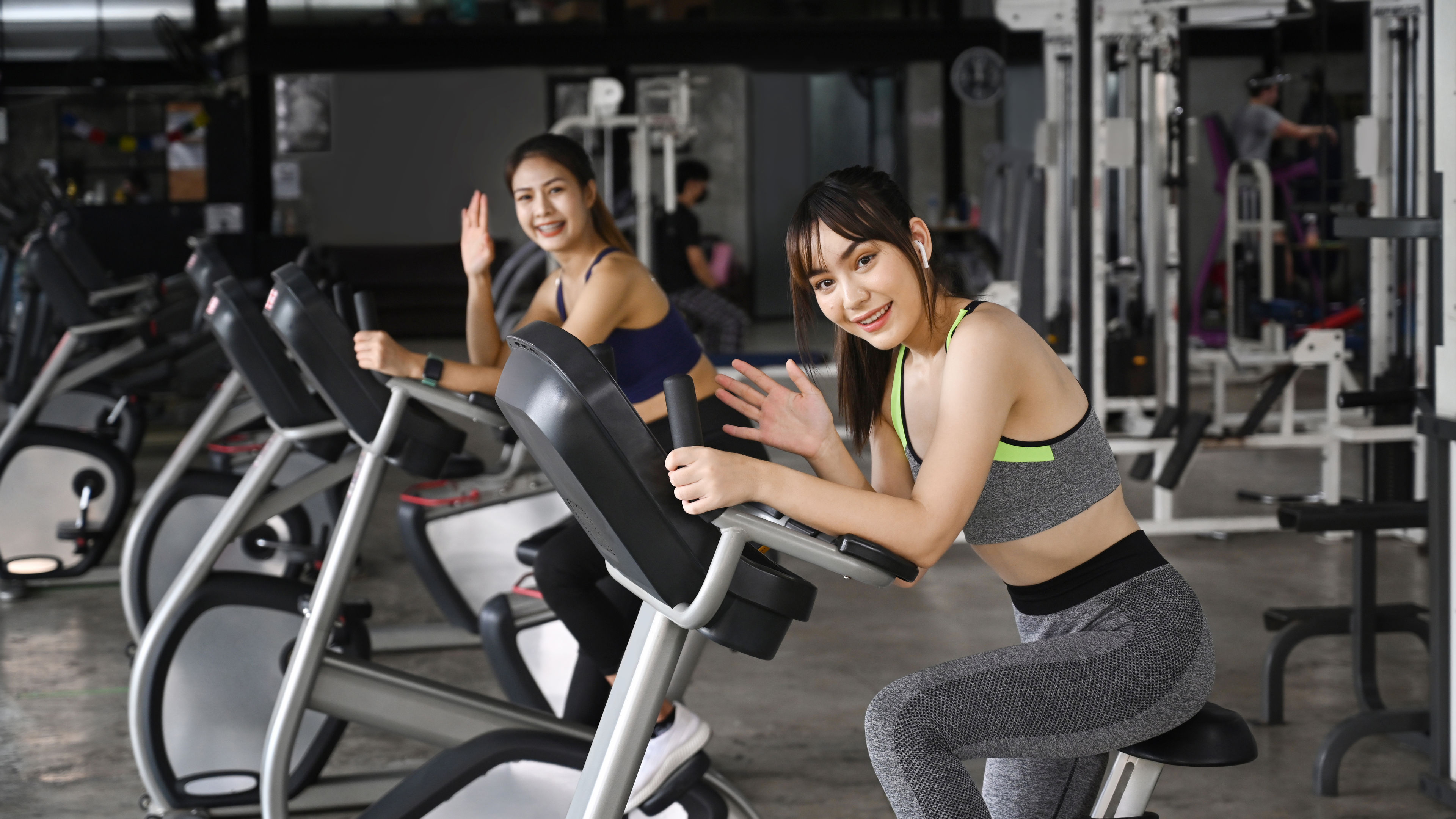 Two fitness women in sportswear are exercising on stationary bikes in the gym. 