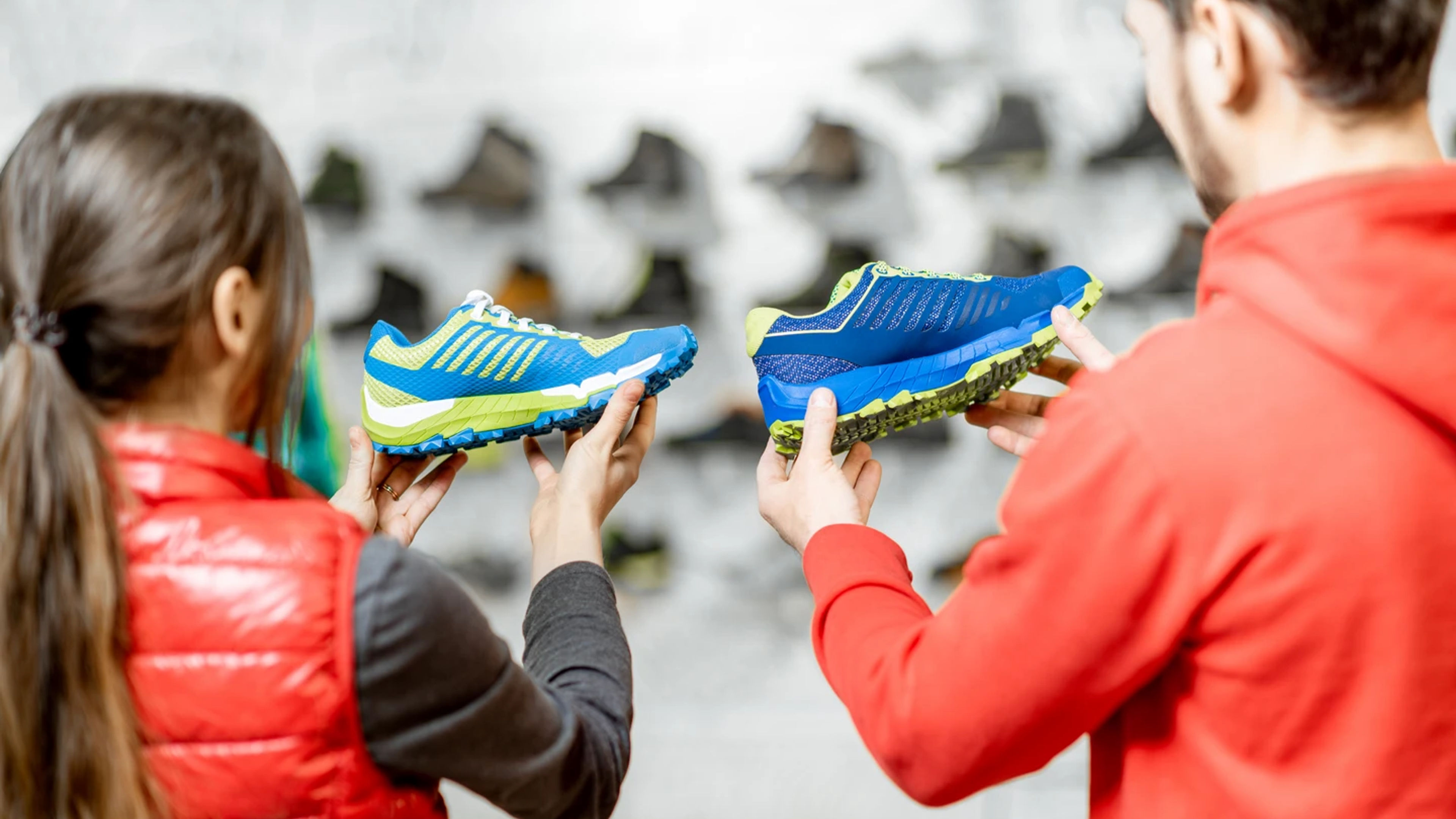 A man and a woman in a shoe store compare two blue and green running shoes while shopping.
