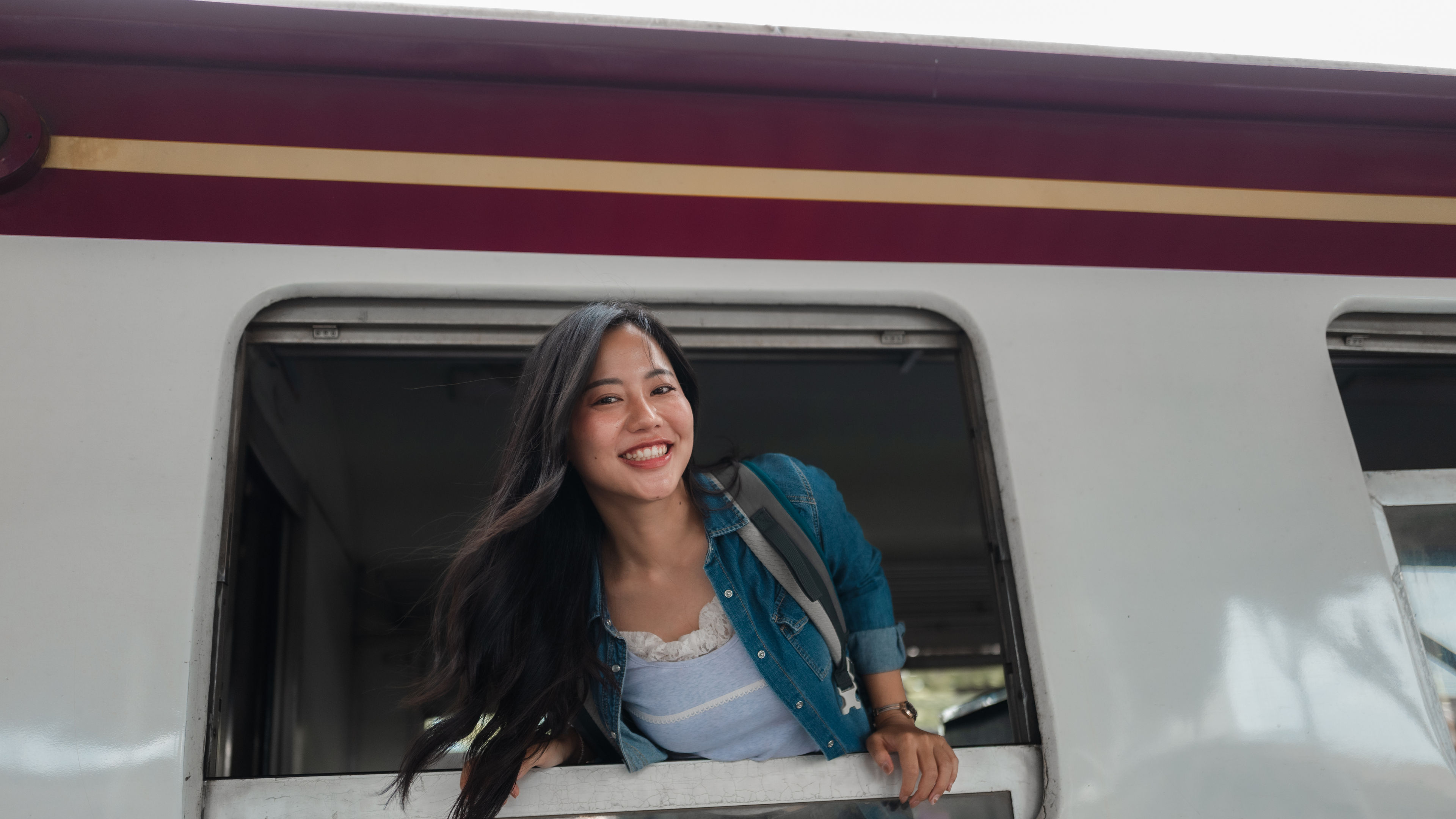 A happy tourist with a backpack looks out the train window, enjoying the view during her trip.