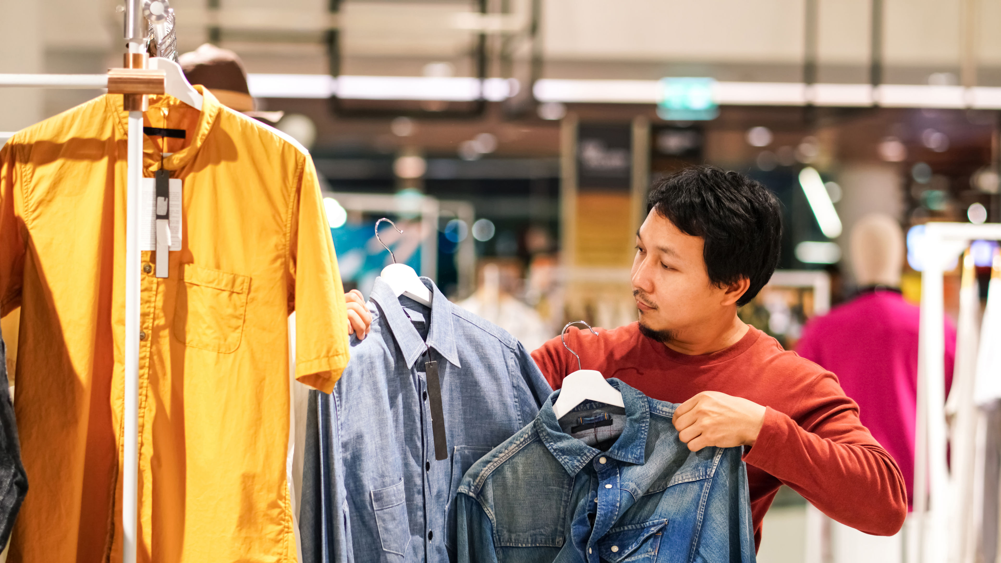 Smart man with beard choosing clothes in clothing store at shopping center.