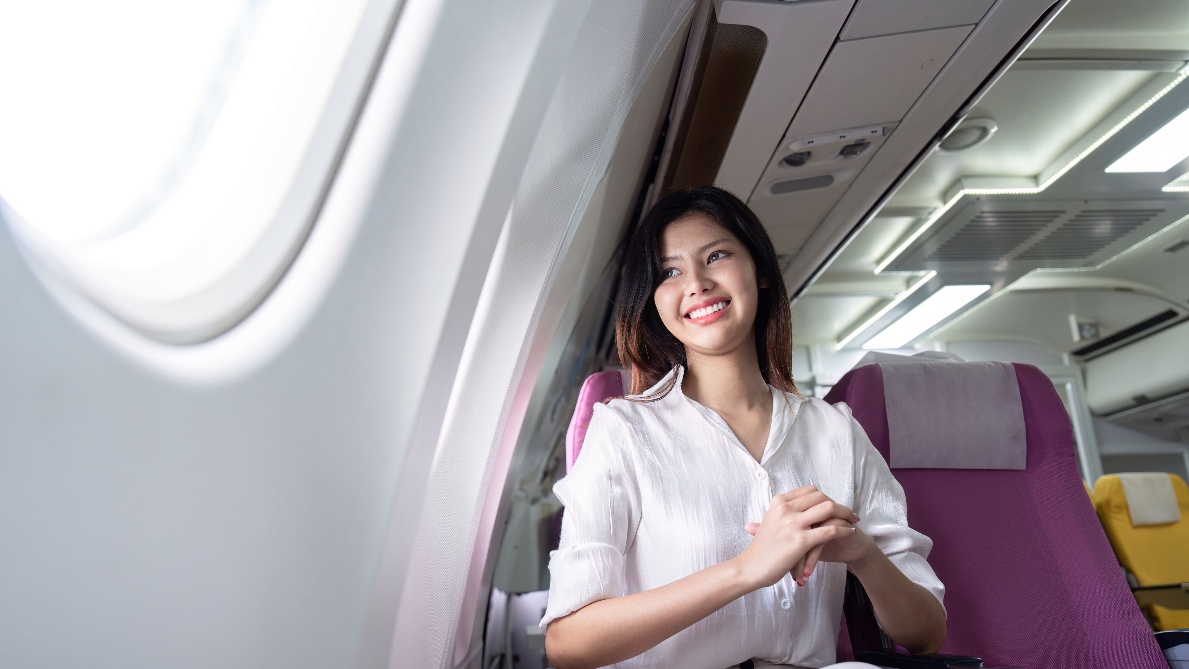 A businesswoman smiling and seated in a comfortable business class seat on an airplane, traveling for a business trip. 