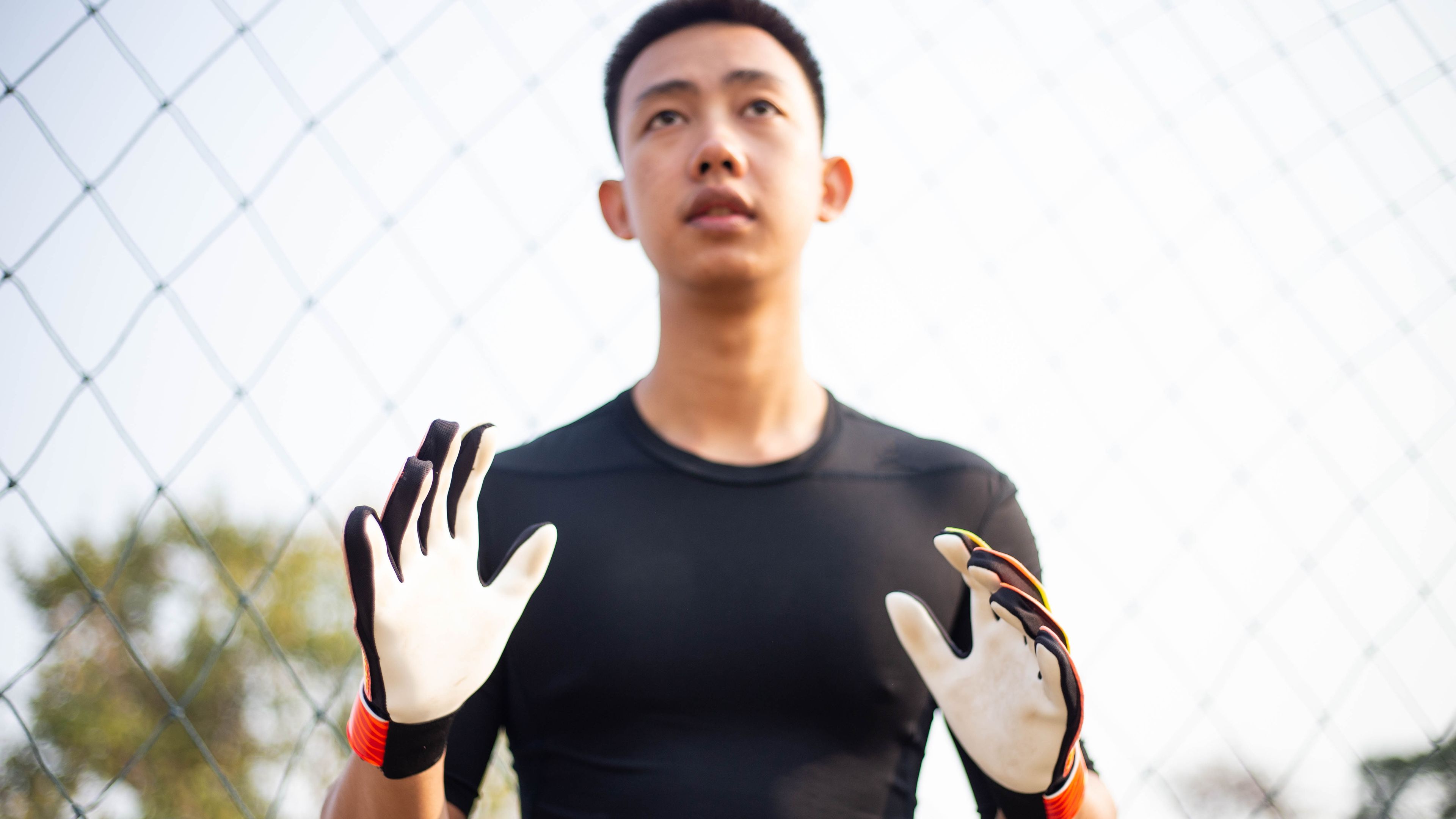 A young man is wearing a black sports shirt and goalkeeper gloves