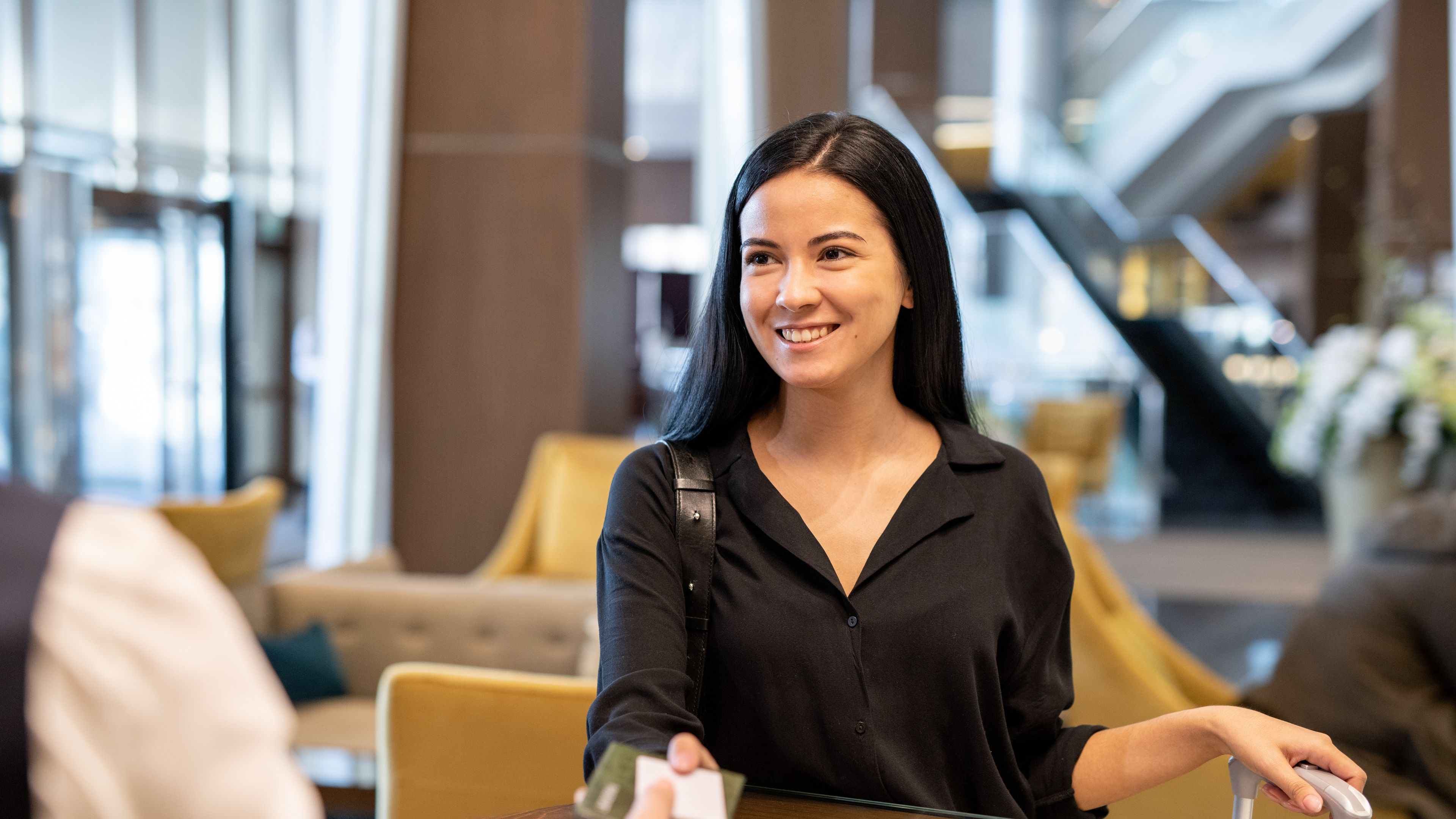 Happy young businesswoman or female traveler with luggage passing documents to hotel receptionist