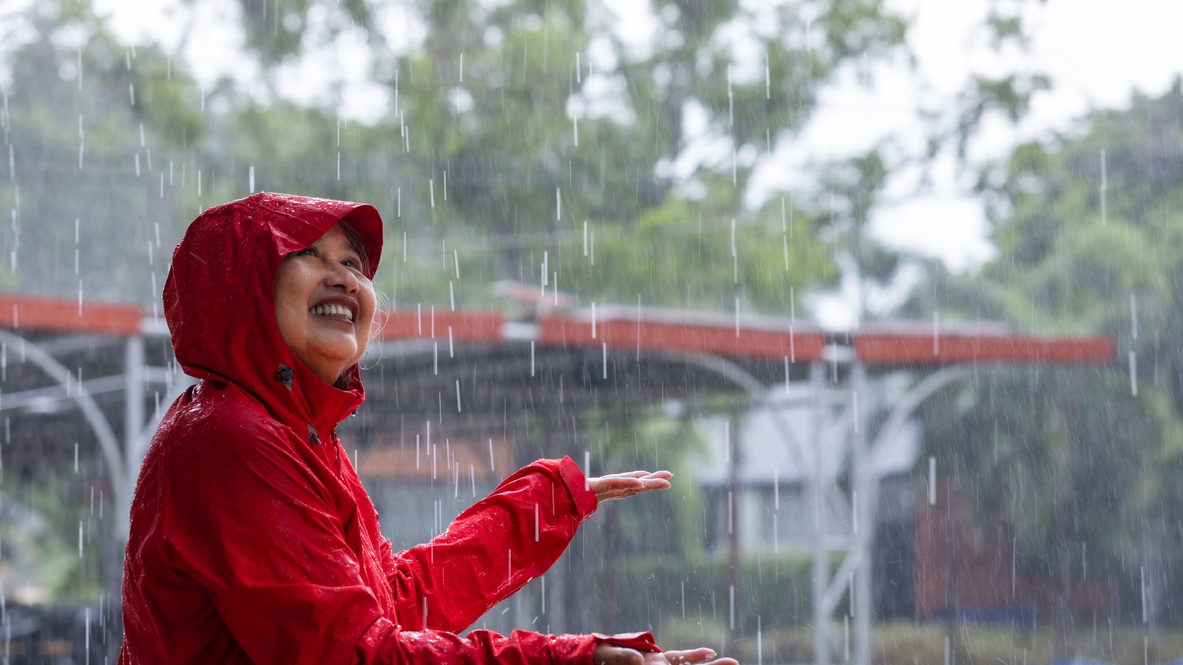 Joyful woman in red raincoat enjoying the rain with outstretched arm, surrounded by nature