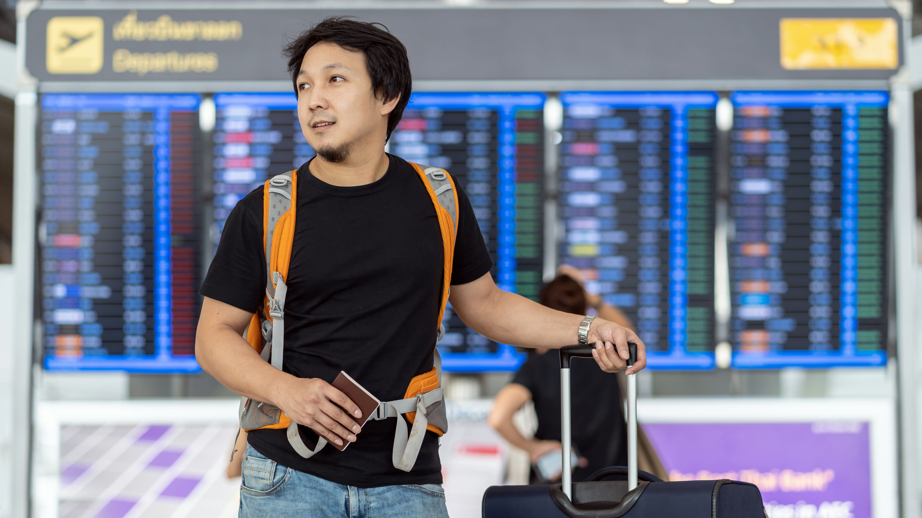 Portrait of Asian traveler with luggage with passport standing over the flight board