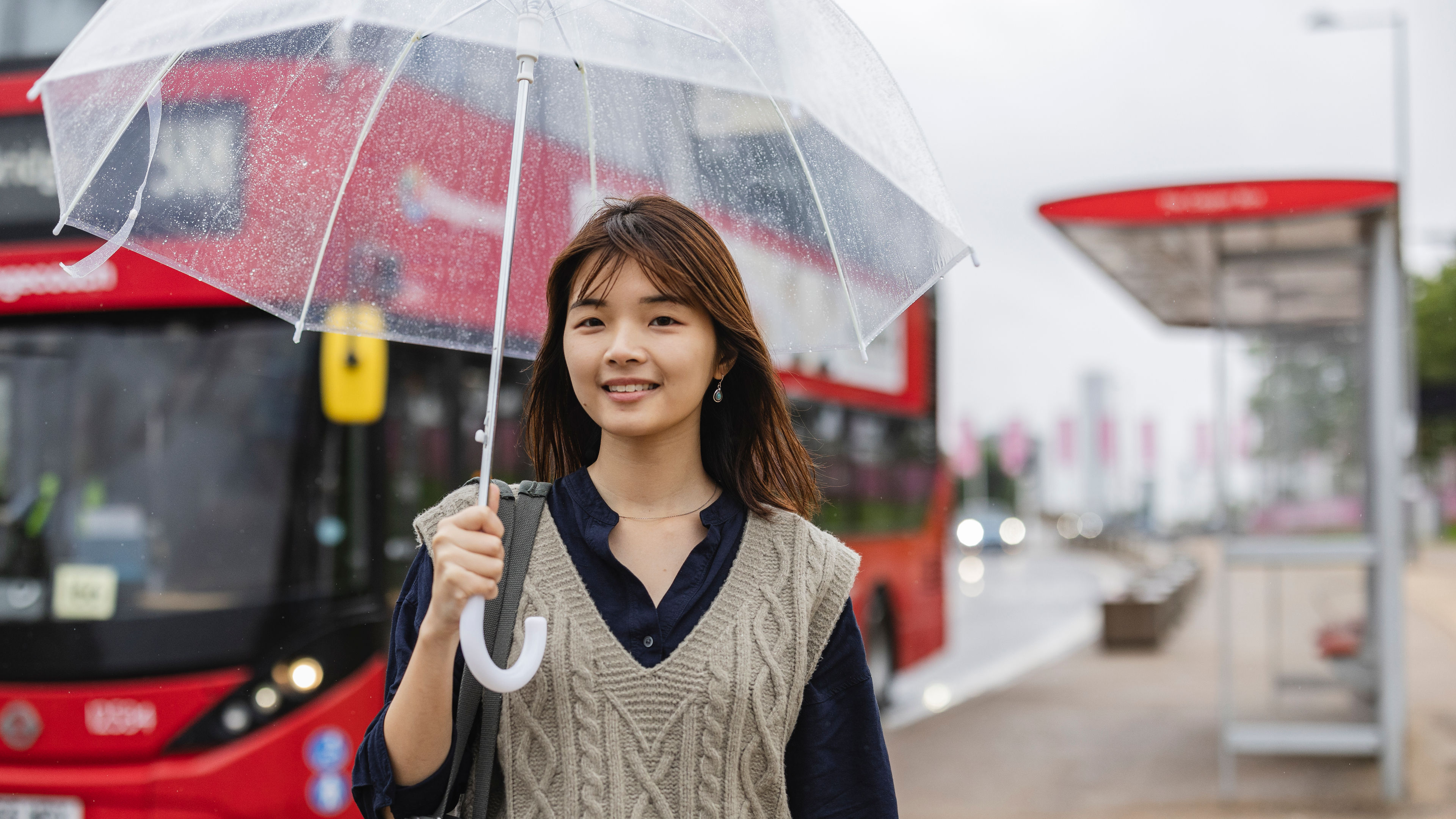 Young woman holding transparent umbrella at london bus stop
