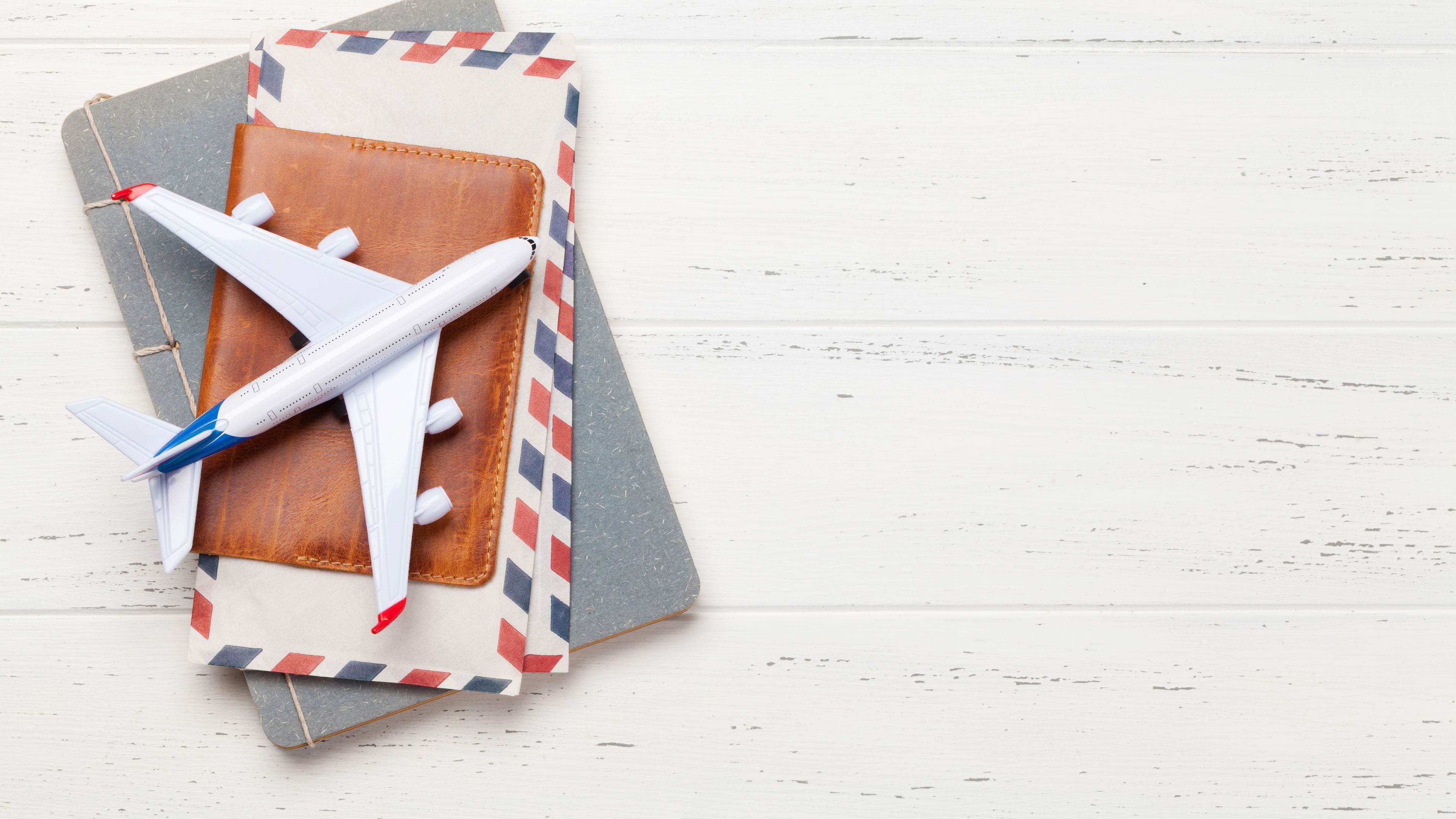 A miniature airplane rests atop a brown leather passport holder, vintage airmail envelopes, and a travel notebook 