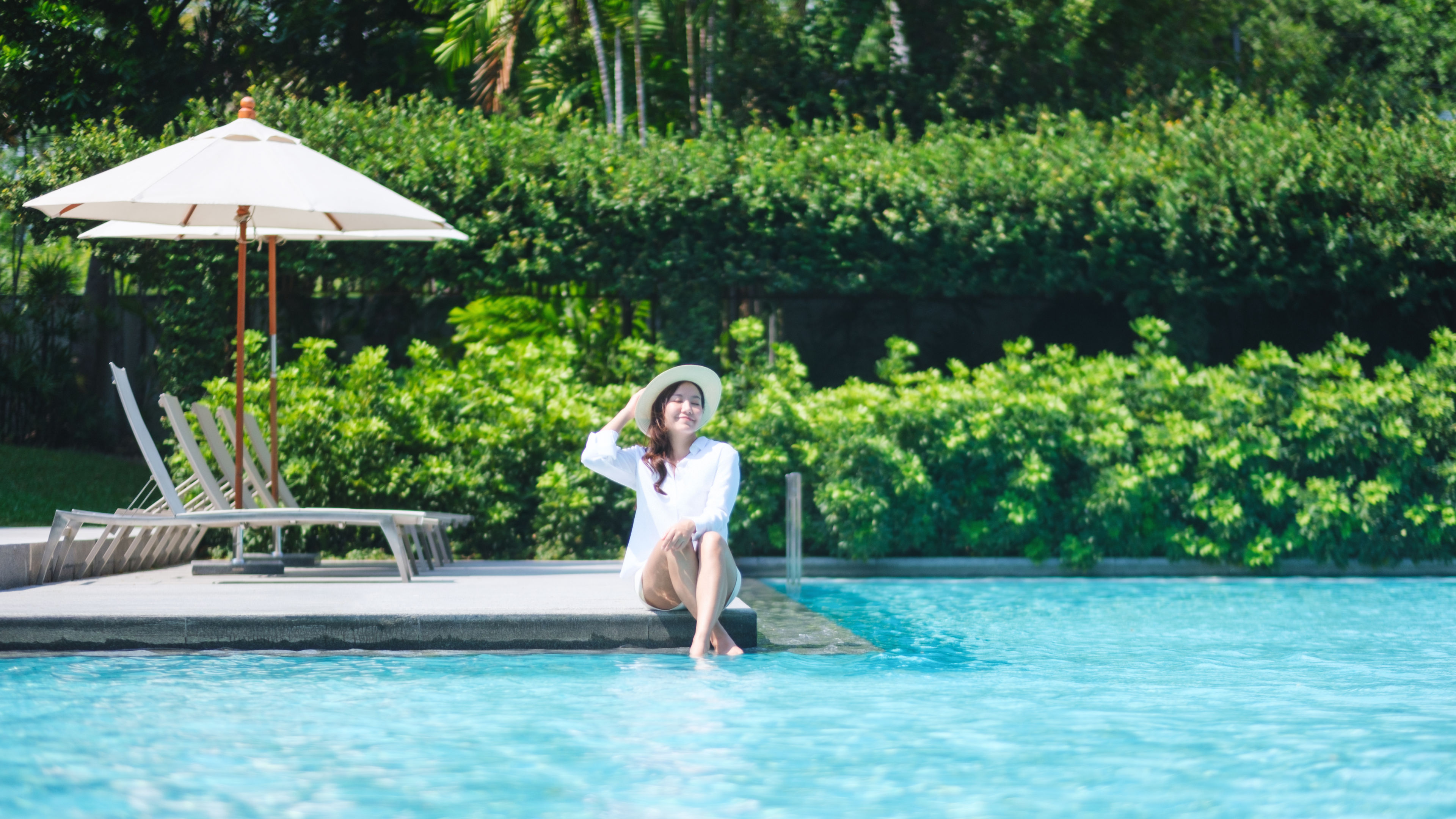 Portrait image of a woman with a hat sitting by the swimming pool