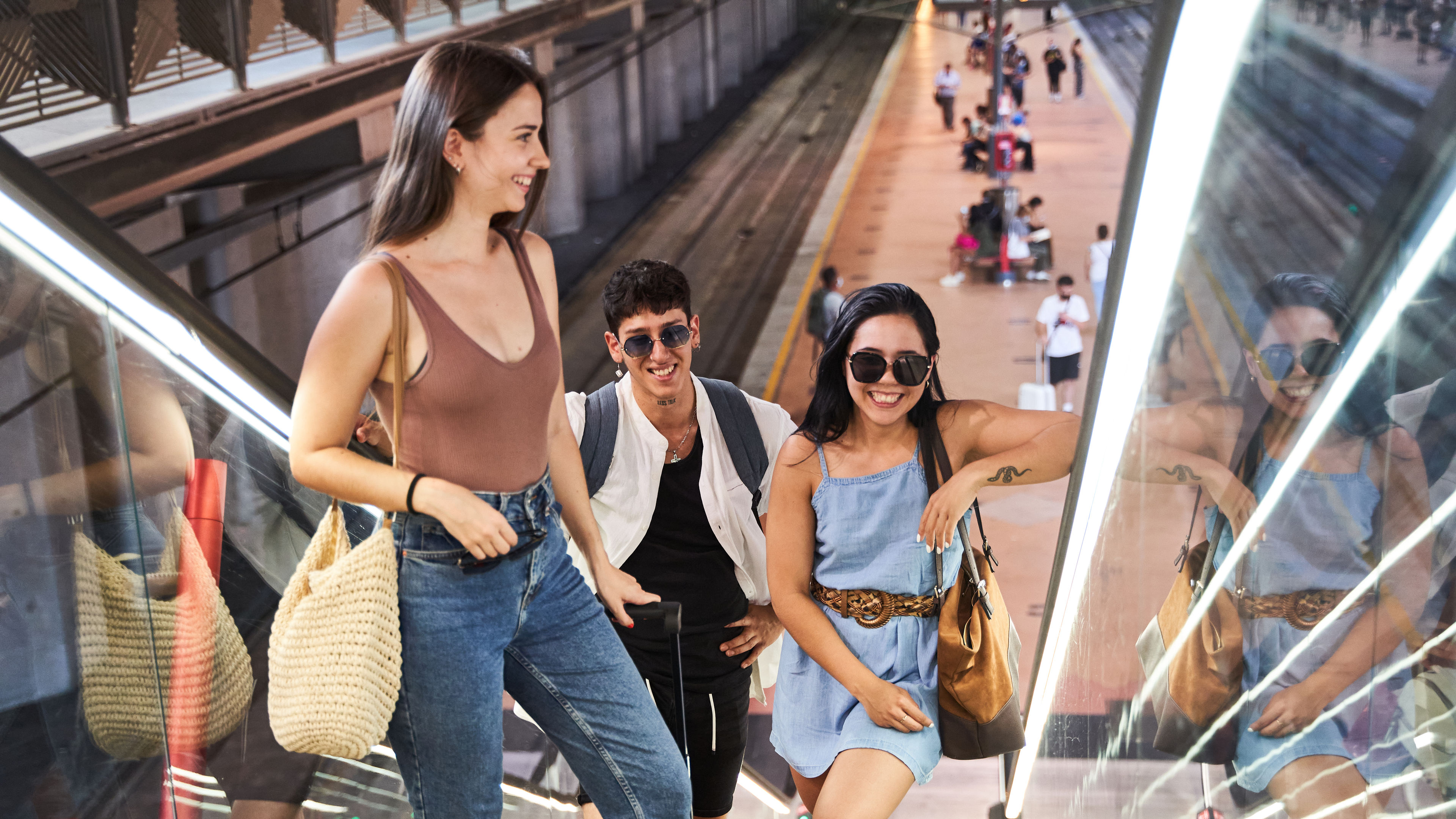 Three people are going up the escalators at the station