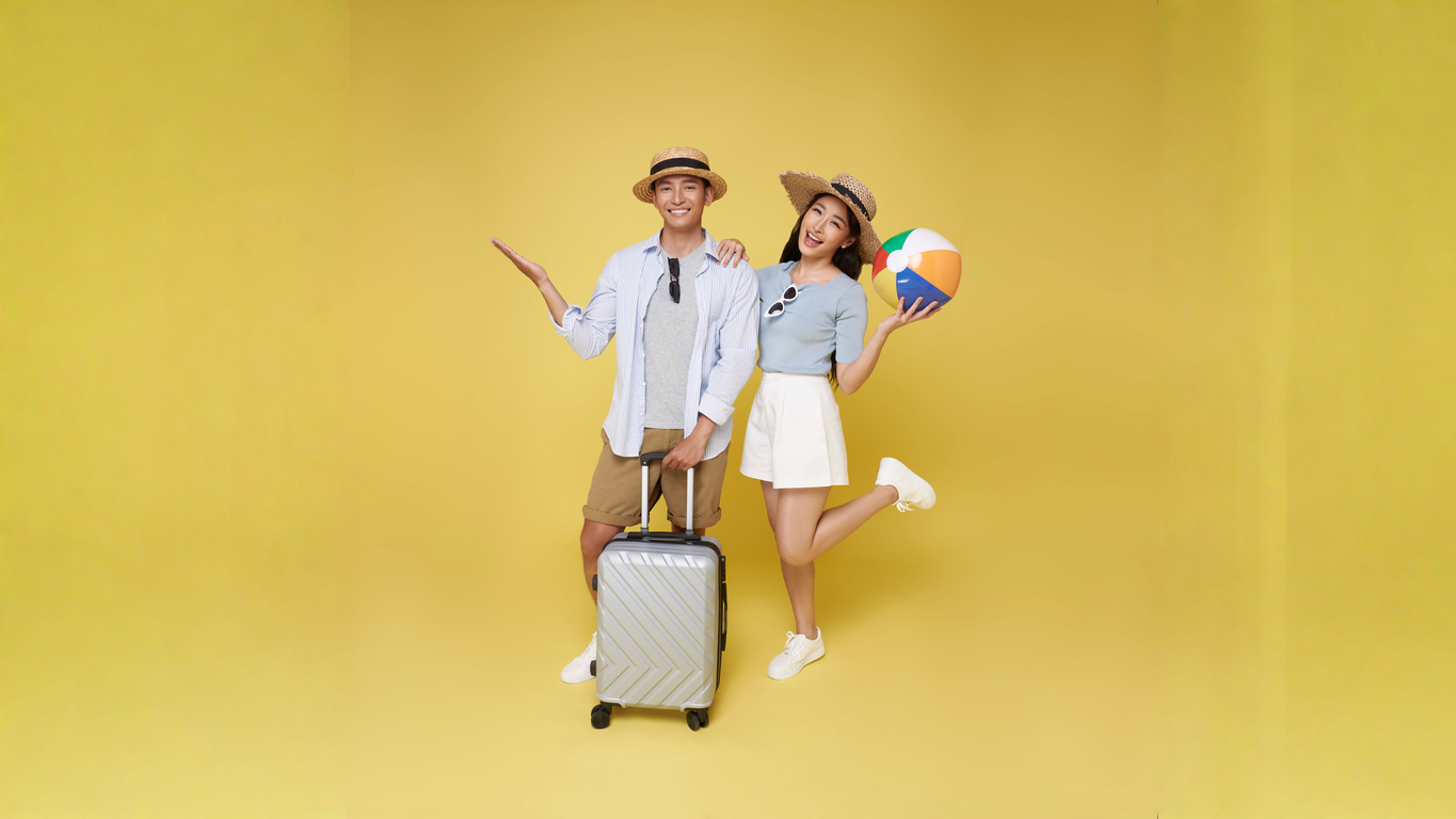 Happy fun Asian couple traveler with suitcase and beach ball isolated on yellow background.