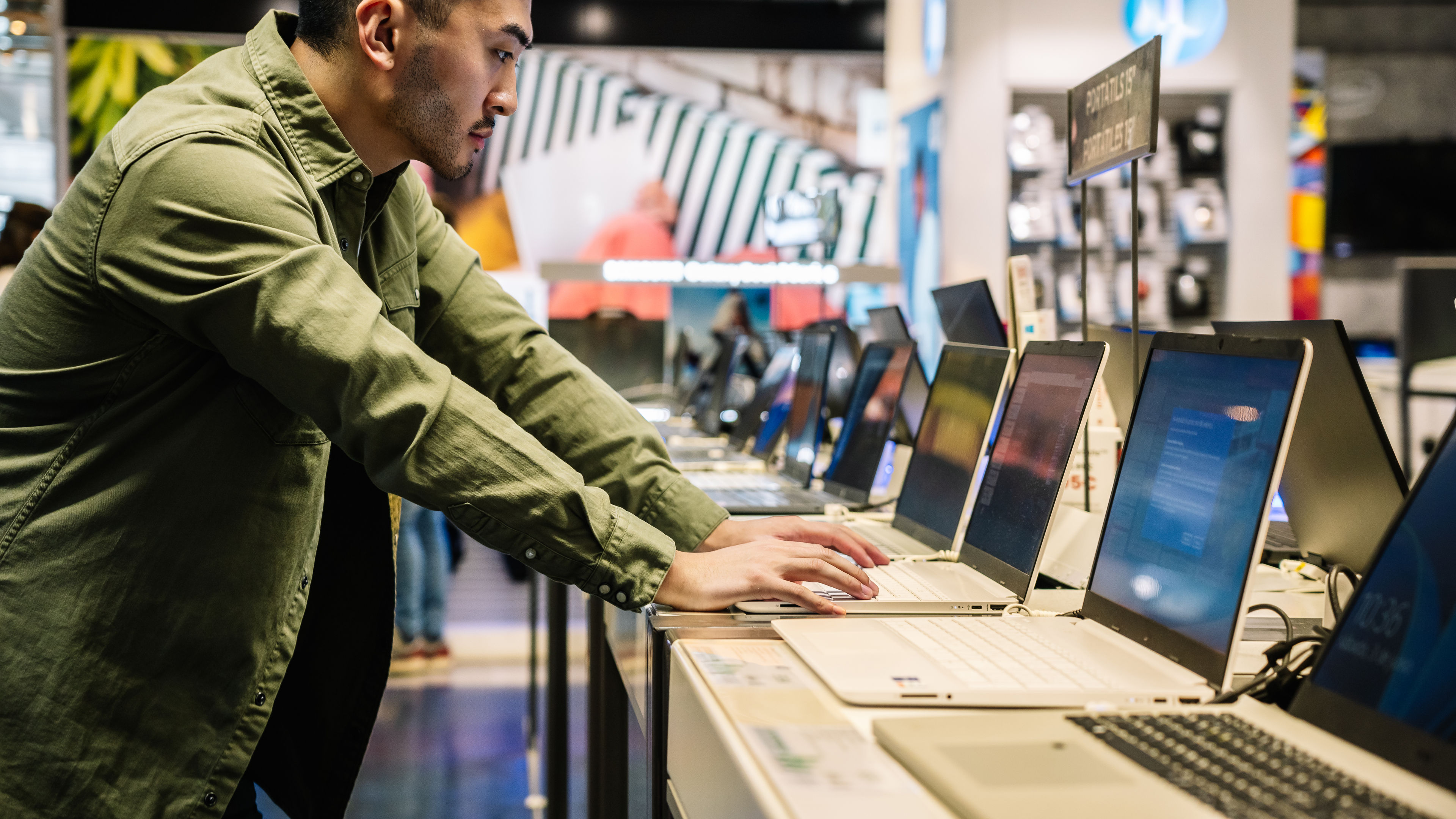 A man browsing and testing laptops in an electronics store.