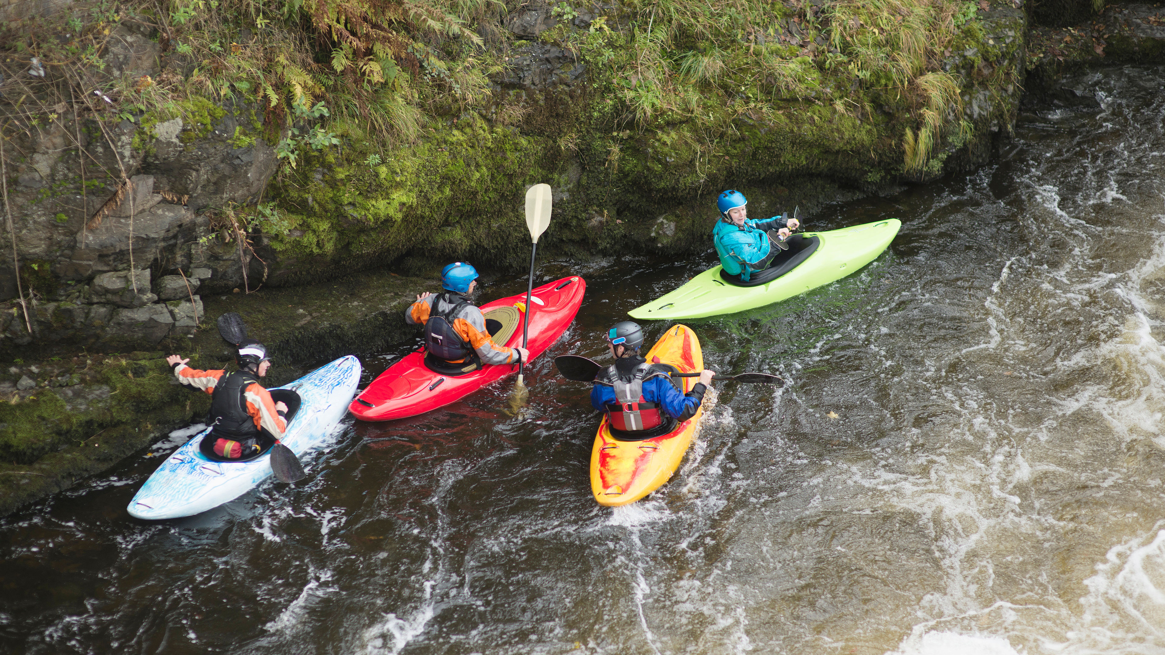 A group of four people in colourful kayaks paddle through a flowing river