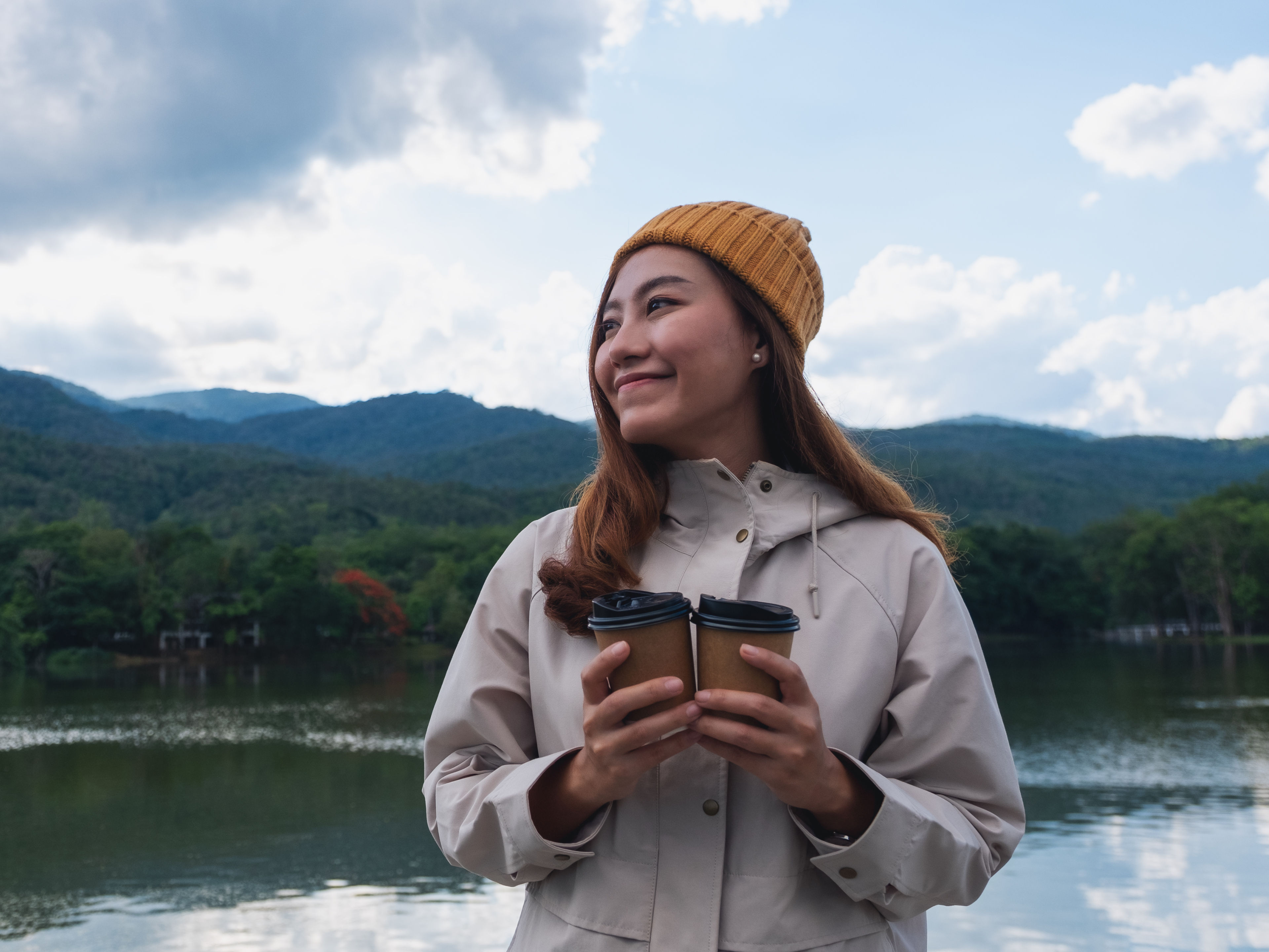 A young woman stands by a calm lake.
