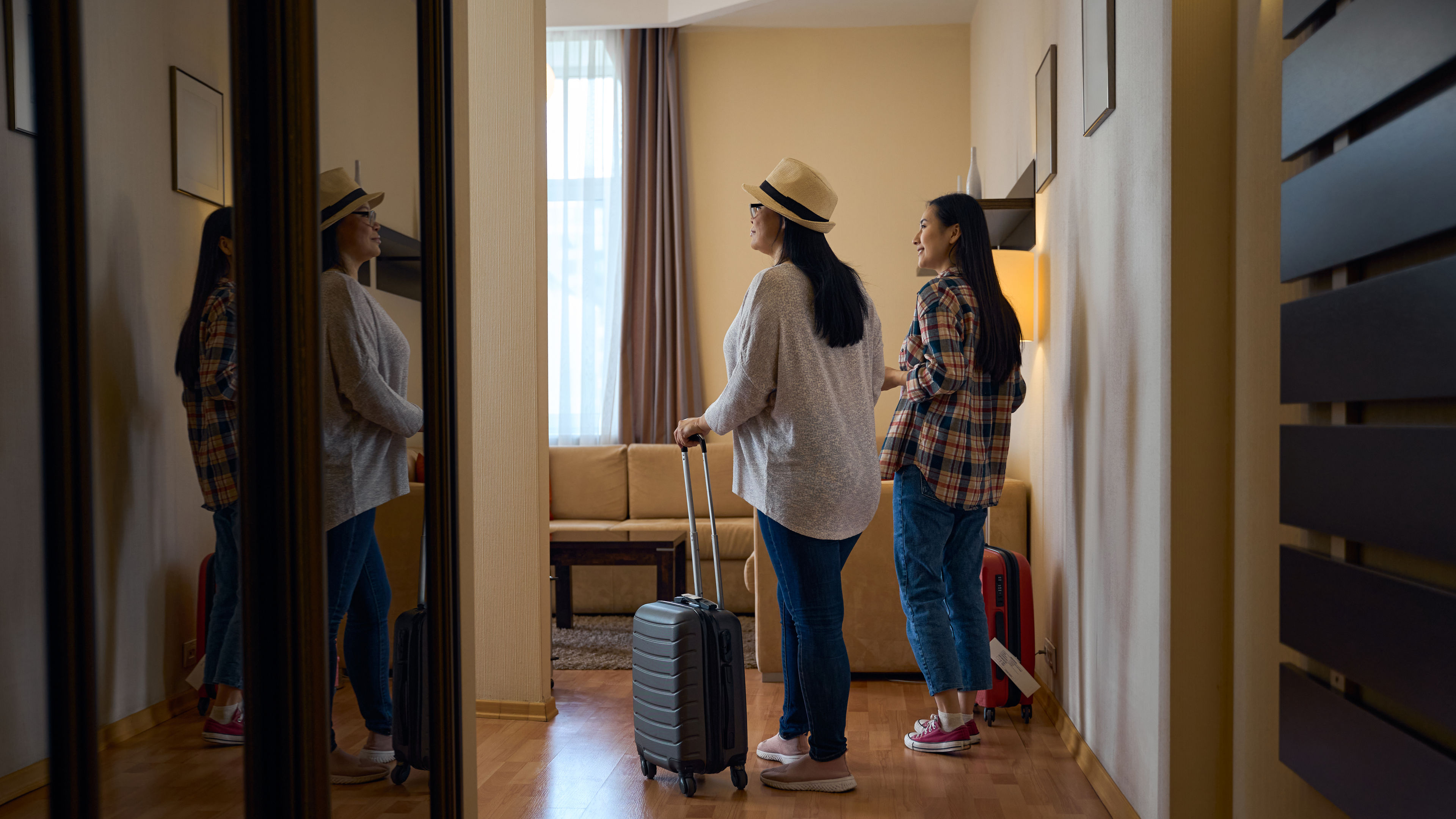 Two women with luggage are exploring their hotel room
