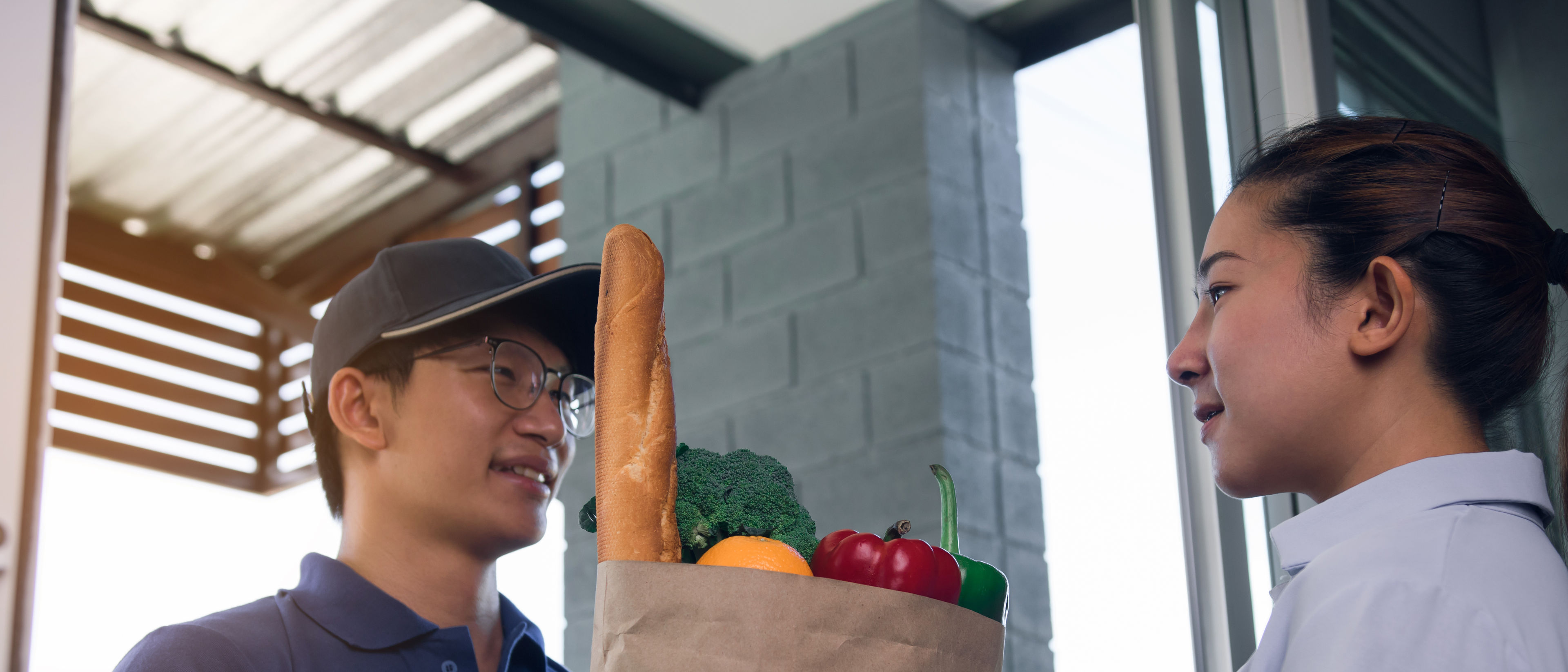 A delivery man handing a paper bag inside  with vegetables