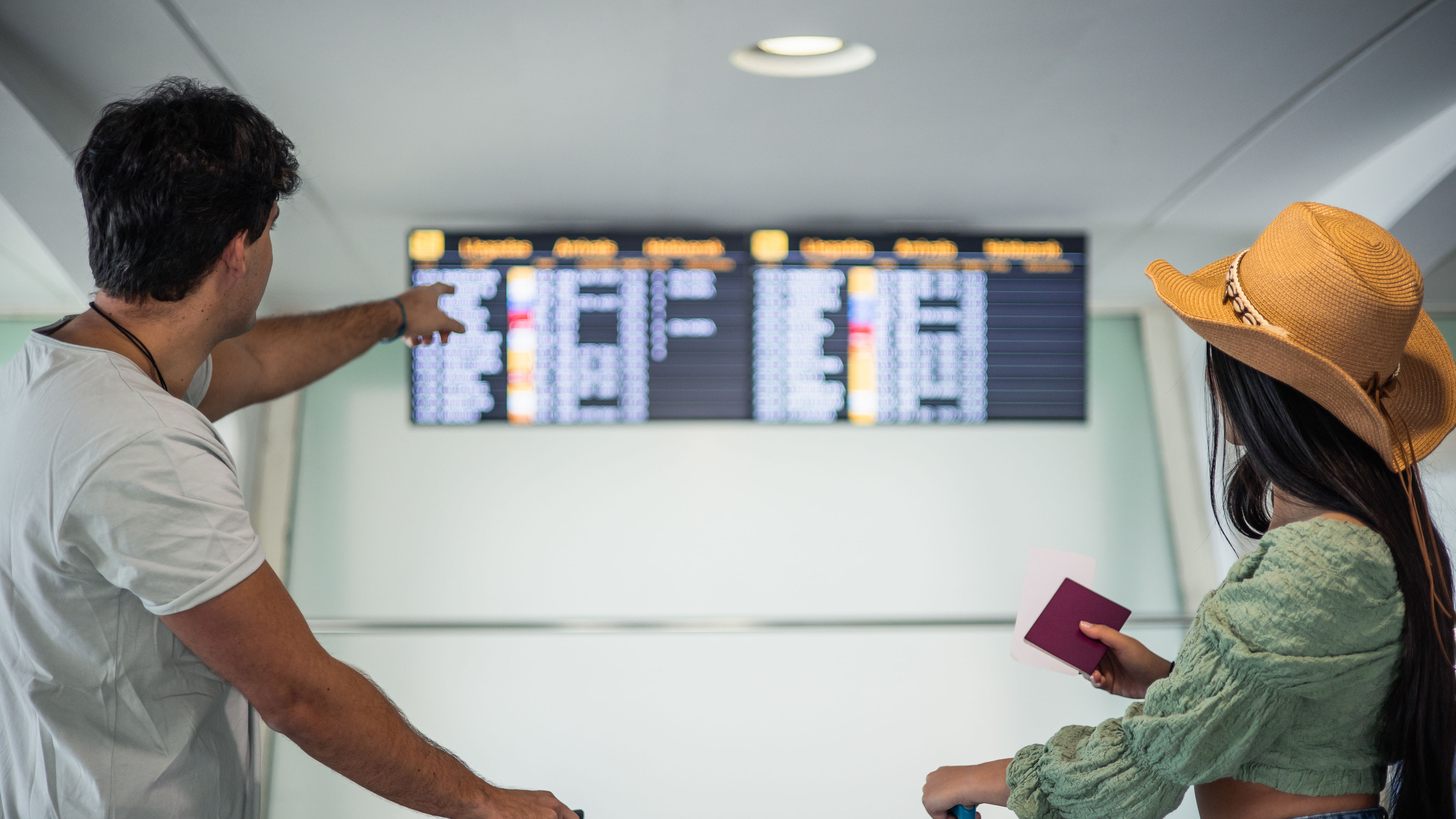 Multicultural traveling wedding couple with their luggage looking at information screens.