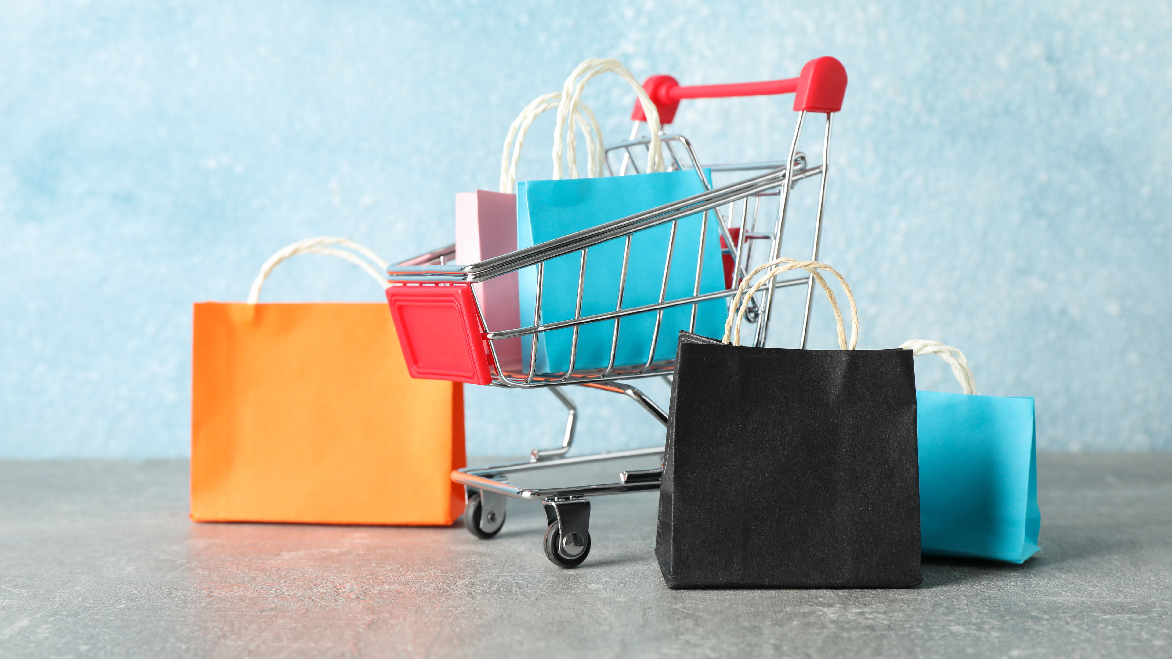Small shopping cart and paper bags on grey background, copy space.