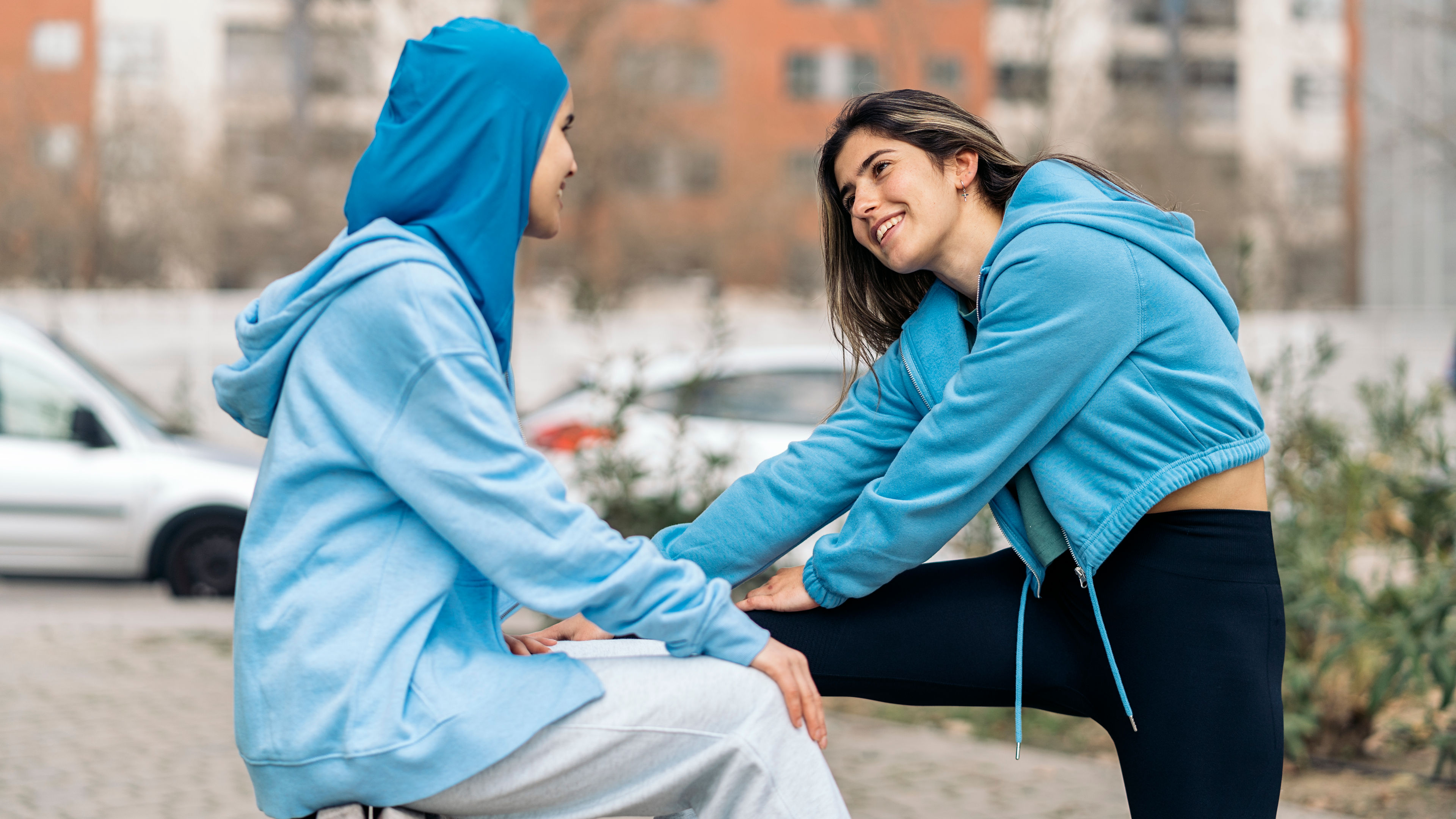 A cheerful woman wearing activewear sitting on a bench in the street with her friend and having fun.