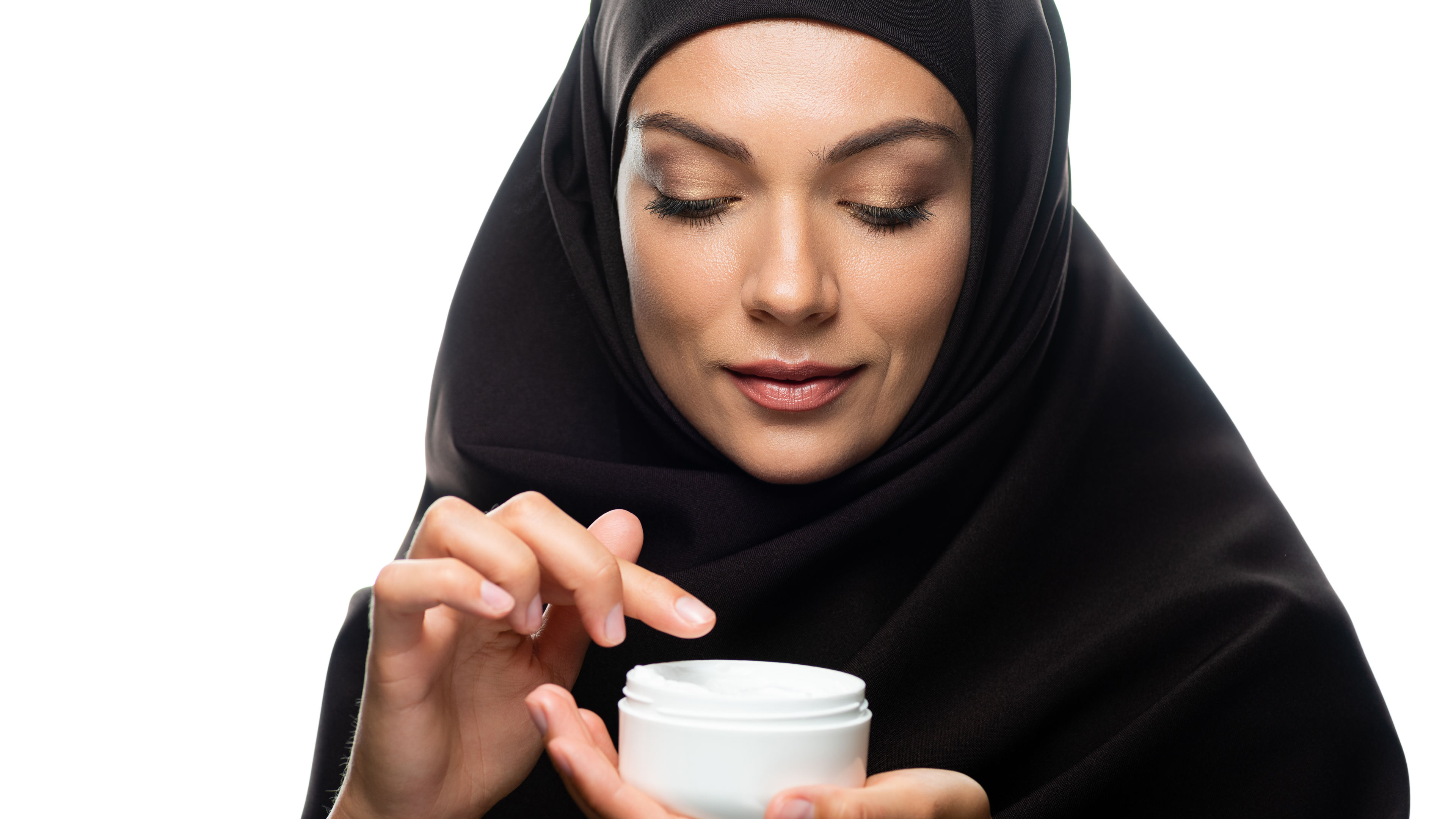Young Muslim woman in hijab holding container with cosmetic cream isolated on white.