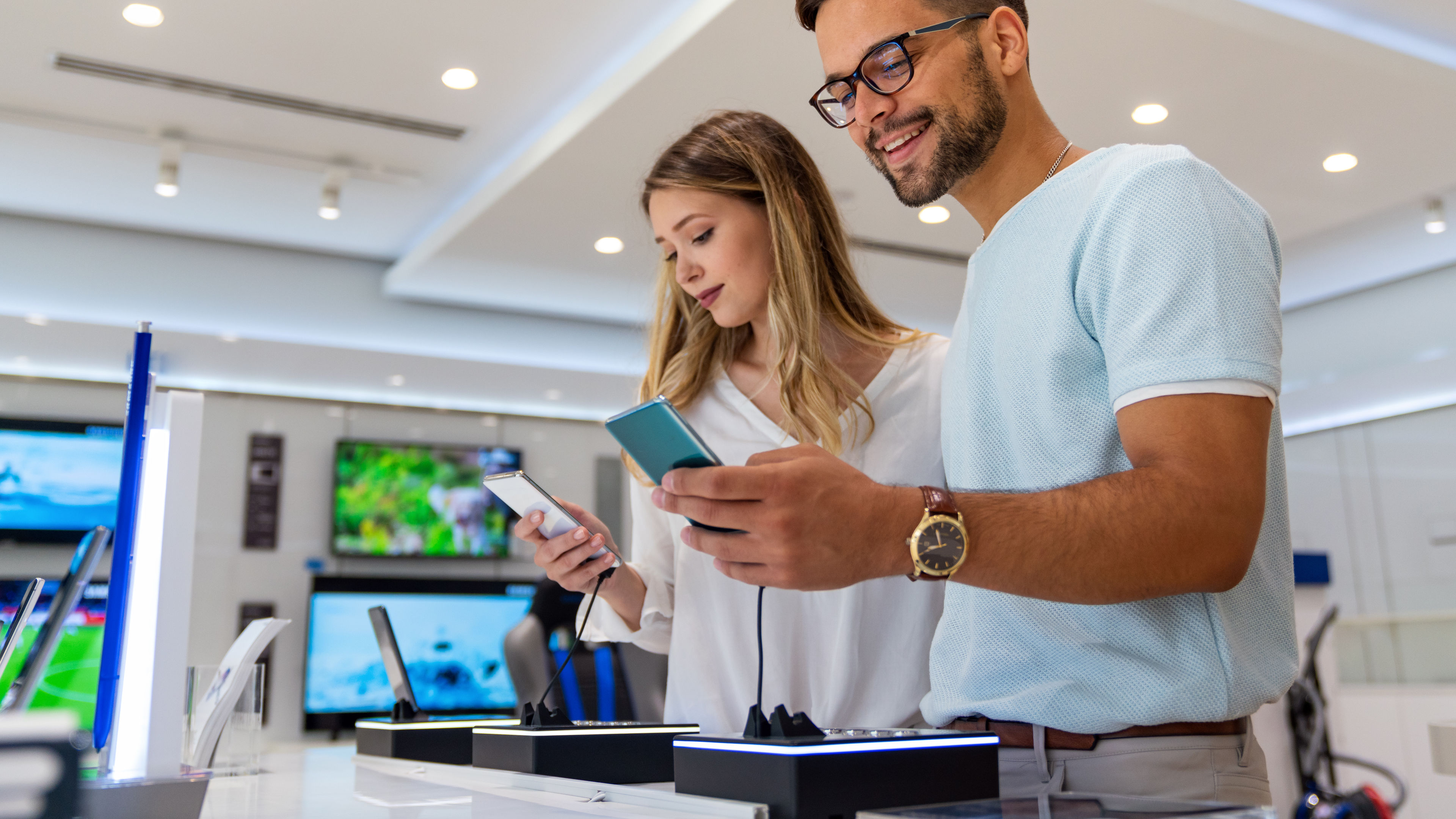 A boy and girl reviewing and choosing mobile phones together inside a mobile shop.