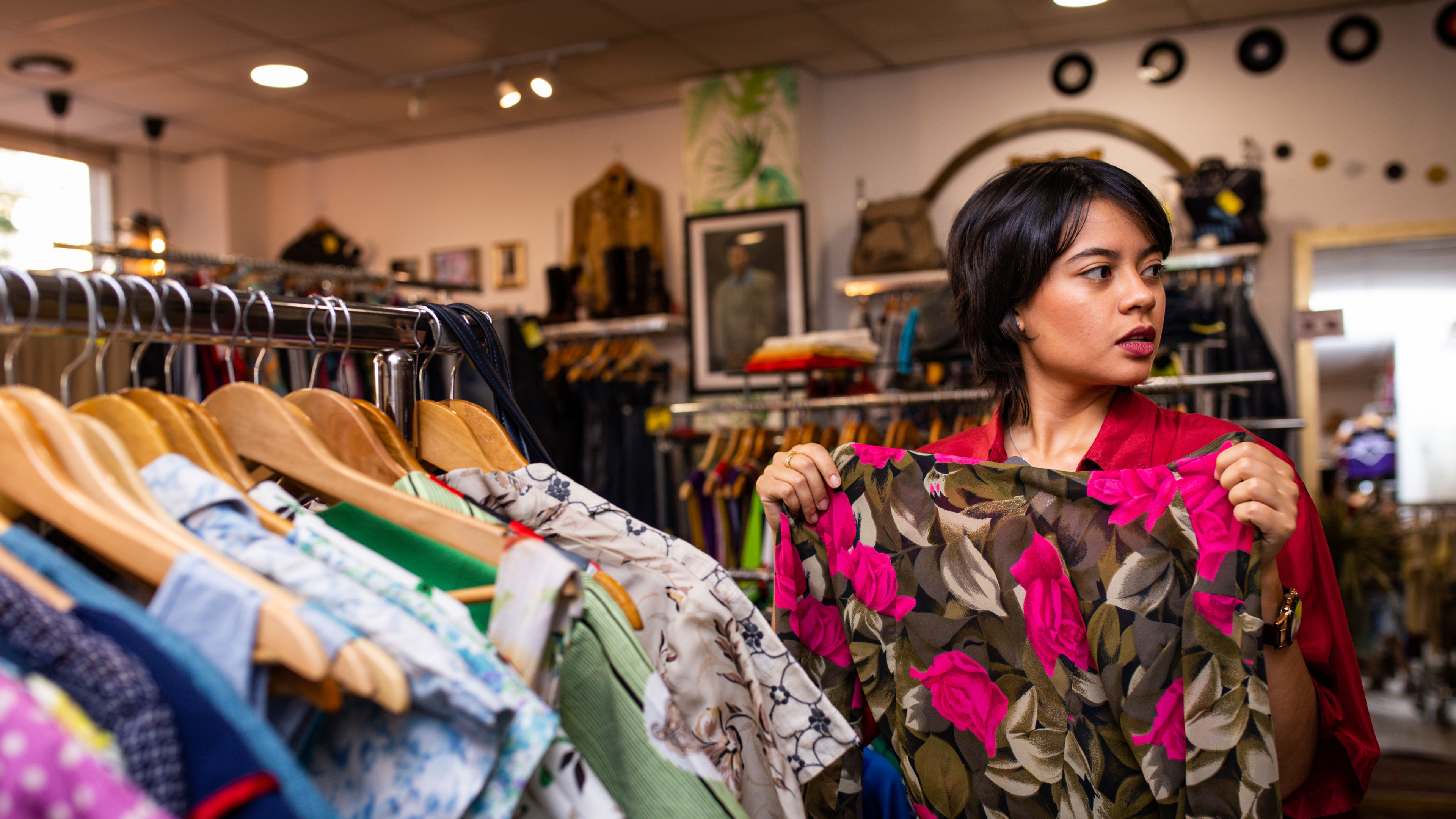A woman browsing through a rack of dresses in a store, holding one up to see if it suits her.