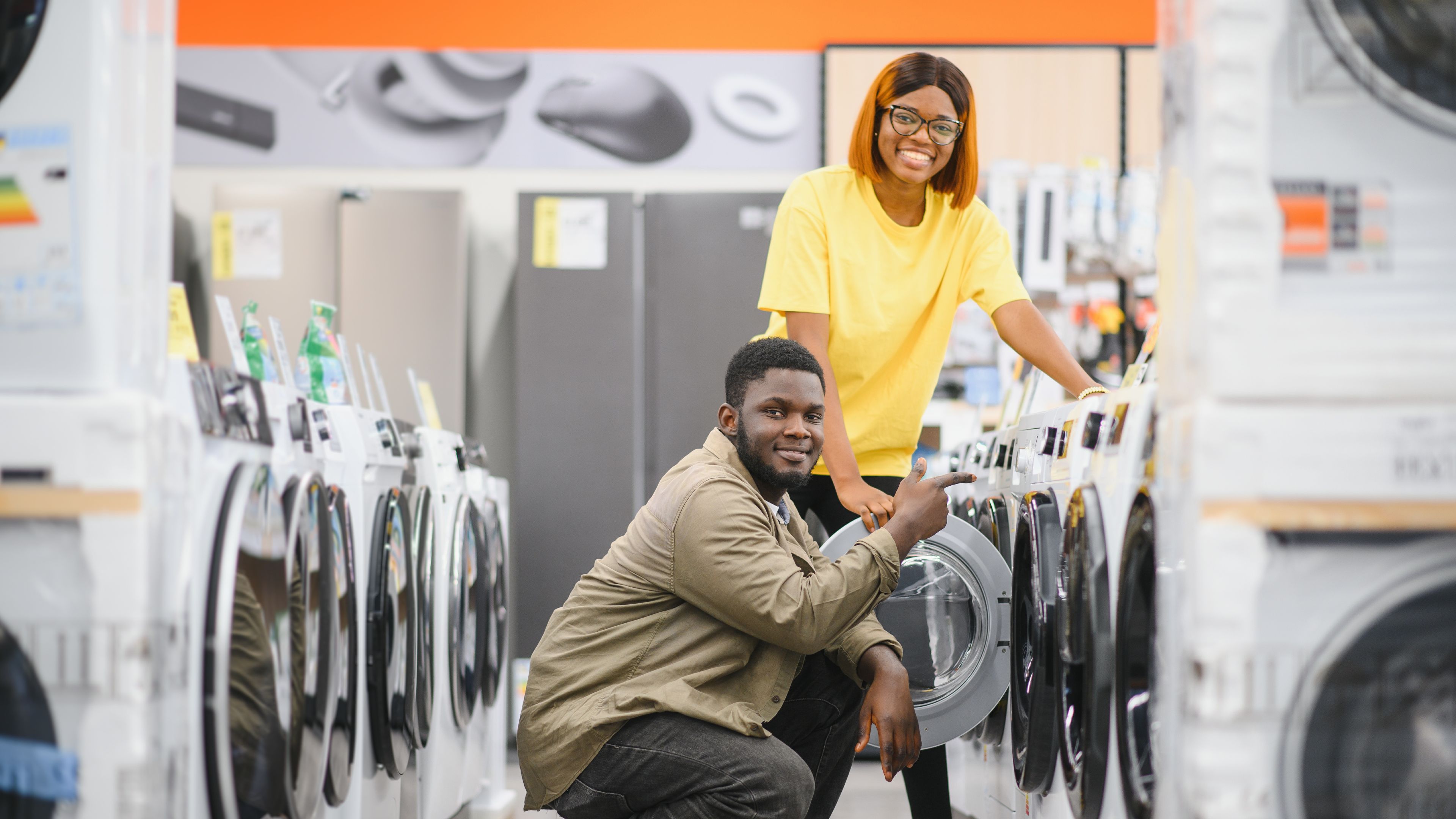 Happy smiling young african american couple choosing washing machine in hypermarket.