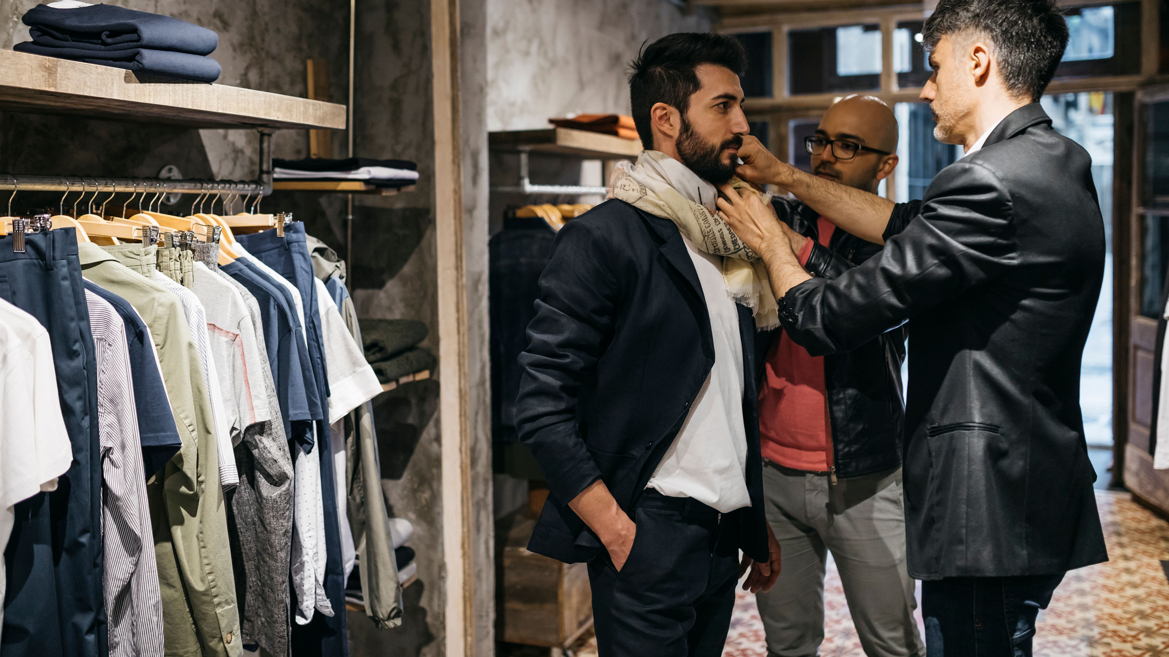 Two men helping another man rearrange or adjust a new jacket inside the clothing store.