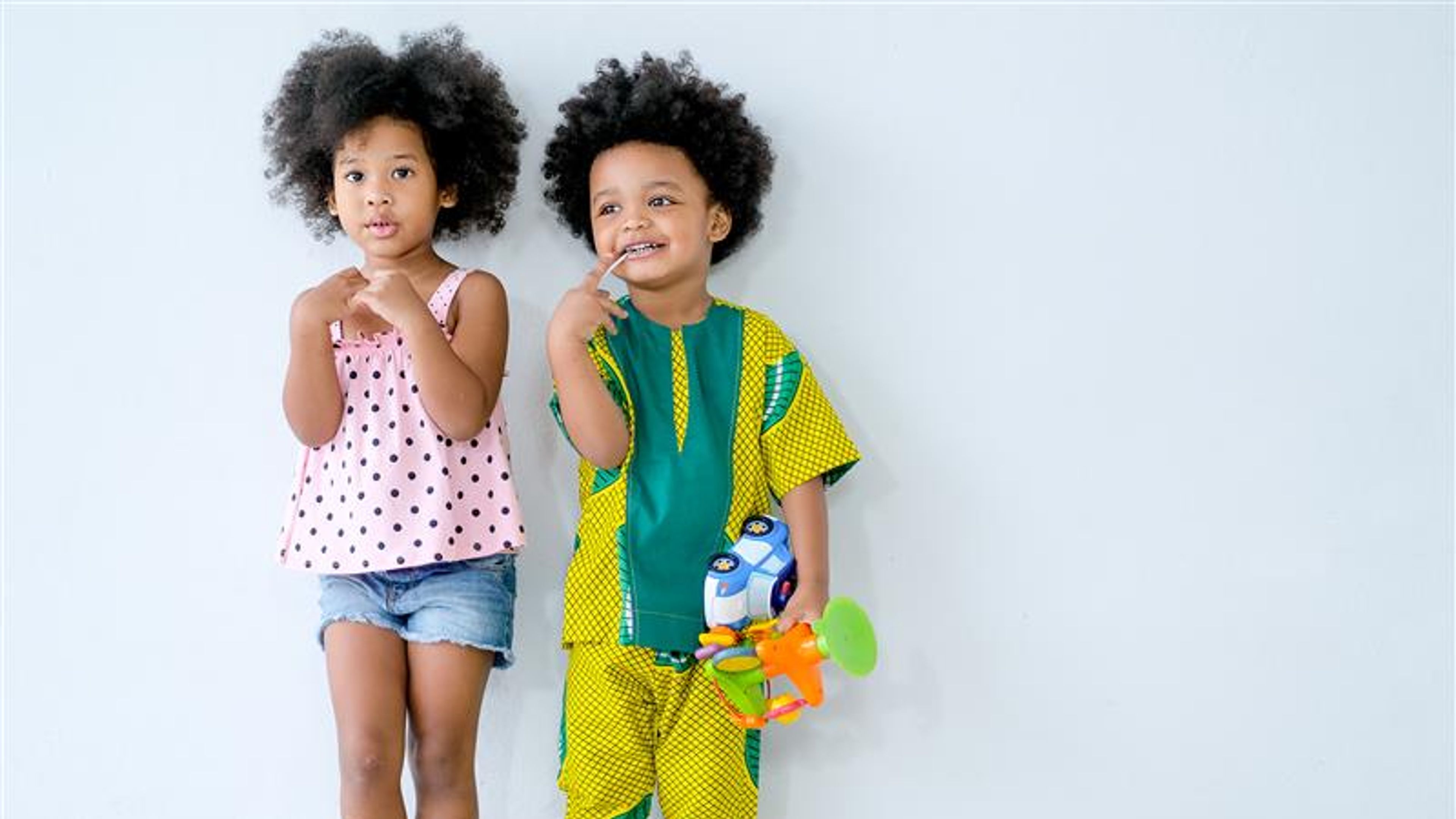 Two young African little boy and girl stand in front of white wall and express different action.