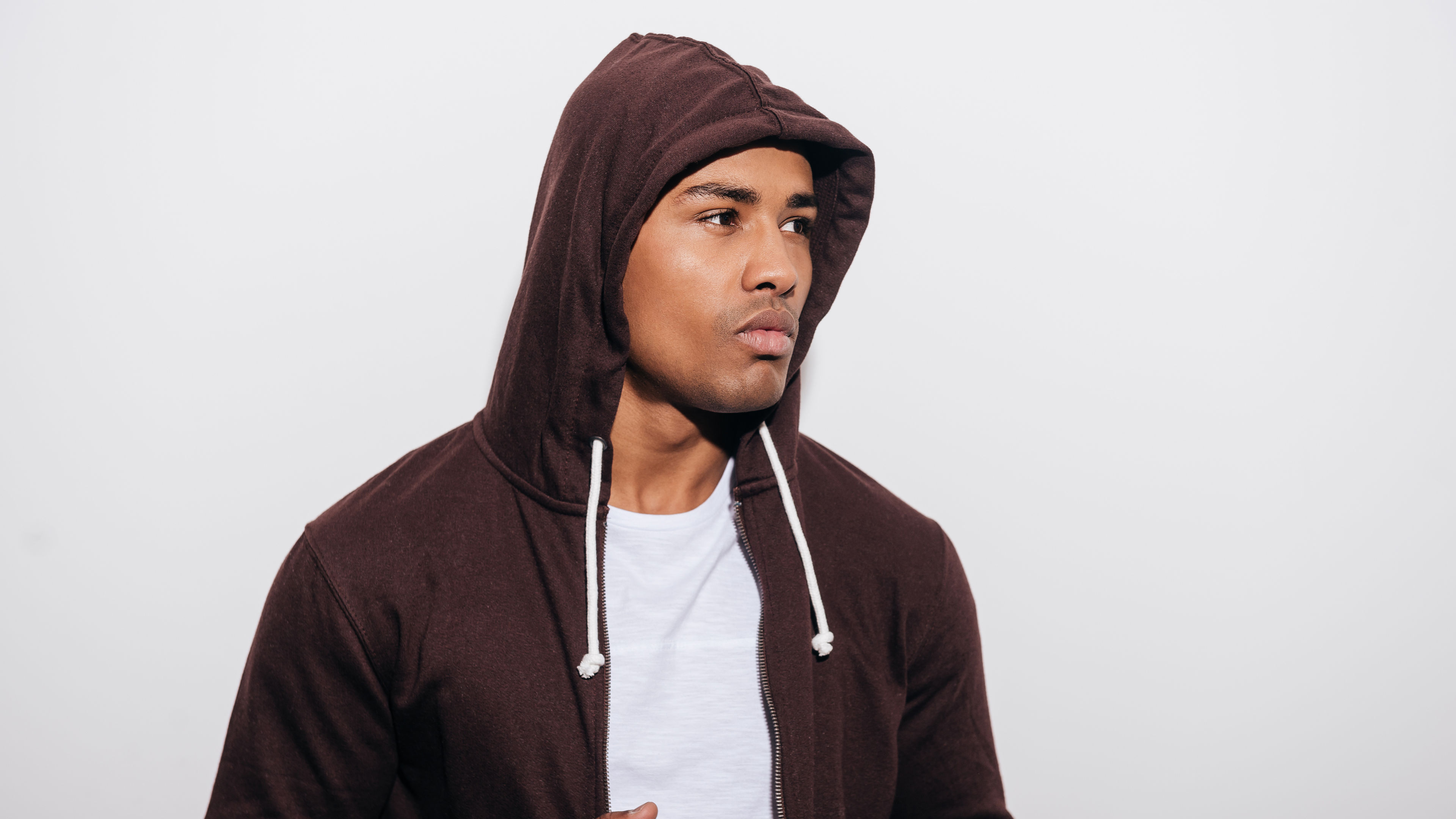 Confident young African man in hooded shirt looking away while standing against white background
