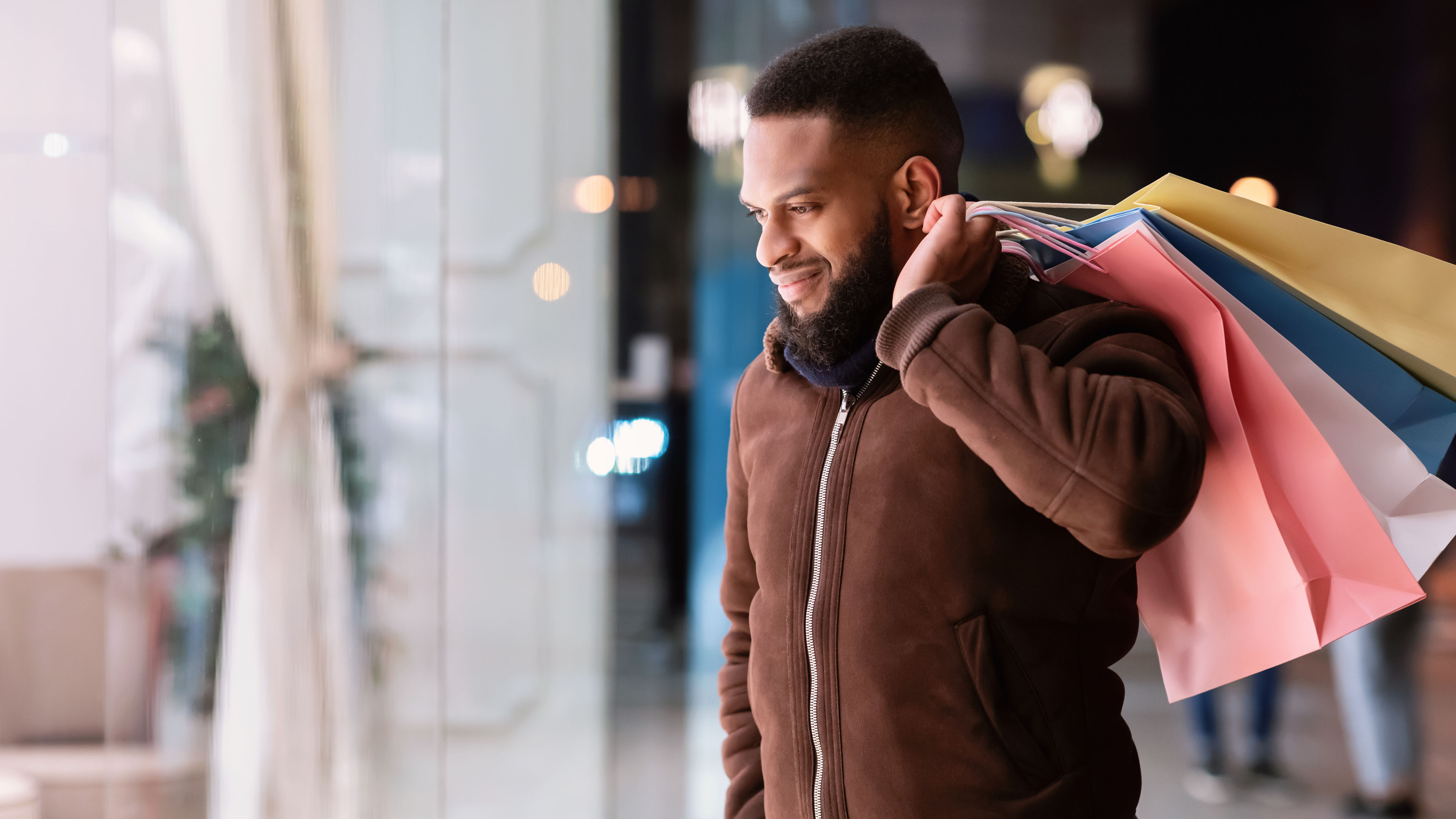Portrait of smiling black bearded guy looking at the shop window of the mall in center