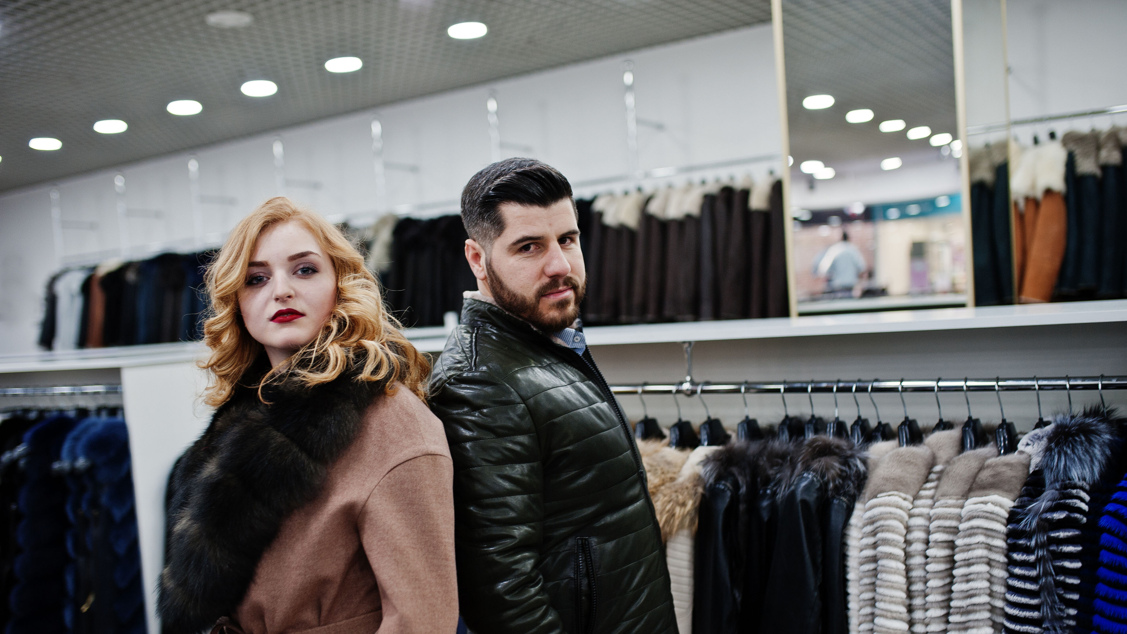 Elegance blonde girl in fur coat and stylish Turkish man at the store of fur coats.