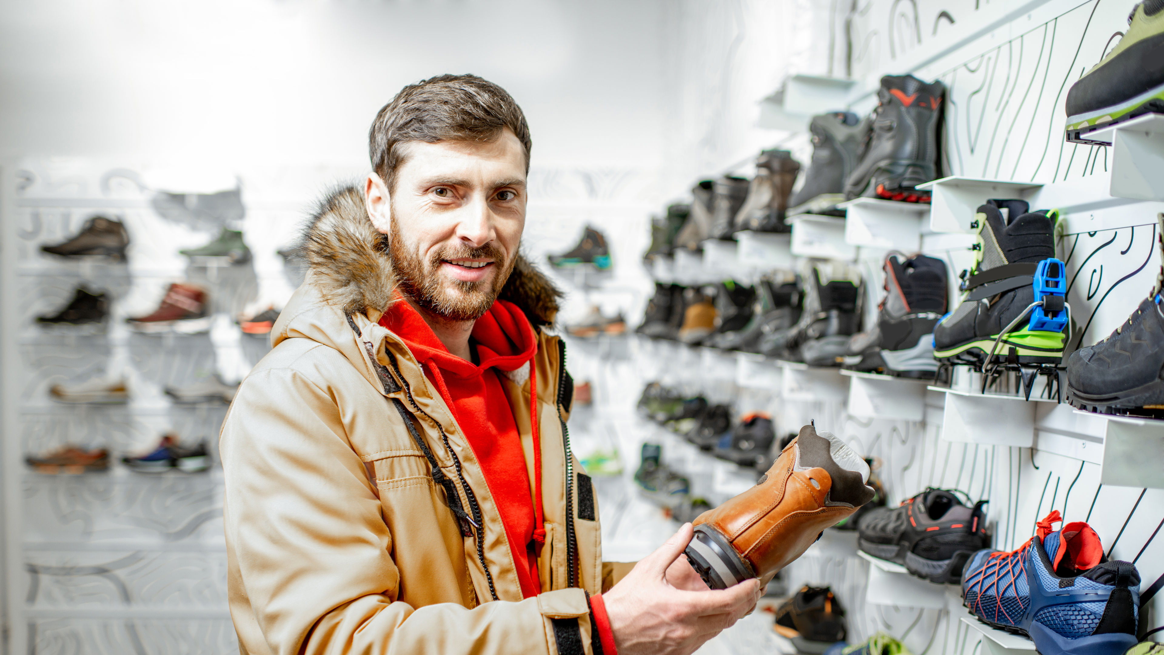 Portrait of a man in winter jacket choosing trail shoes for mountain hiking in the sports shop