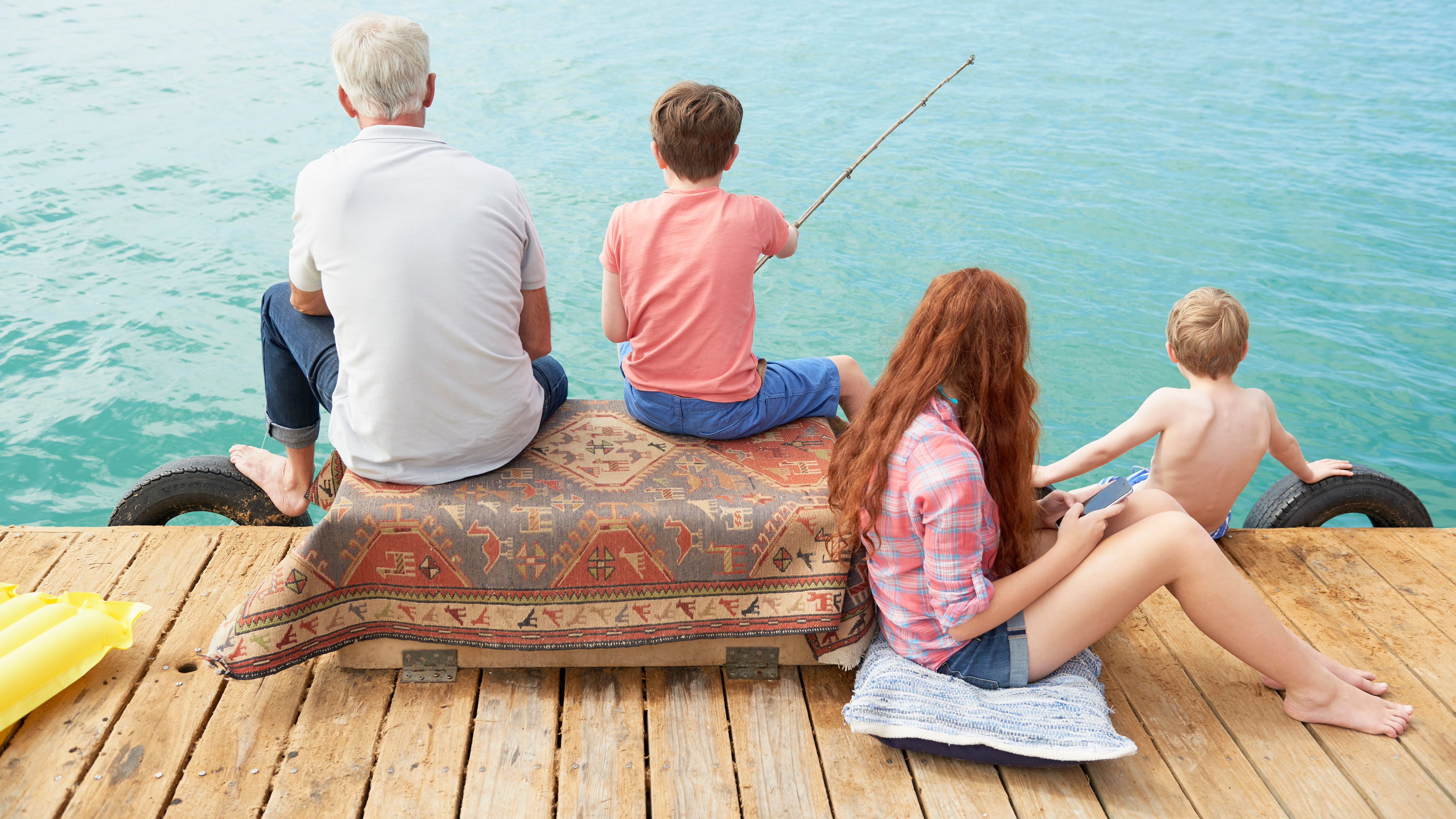 A family of four sits on a wooden dock.  