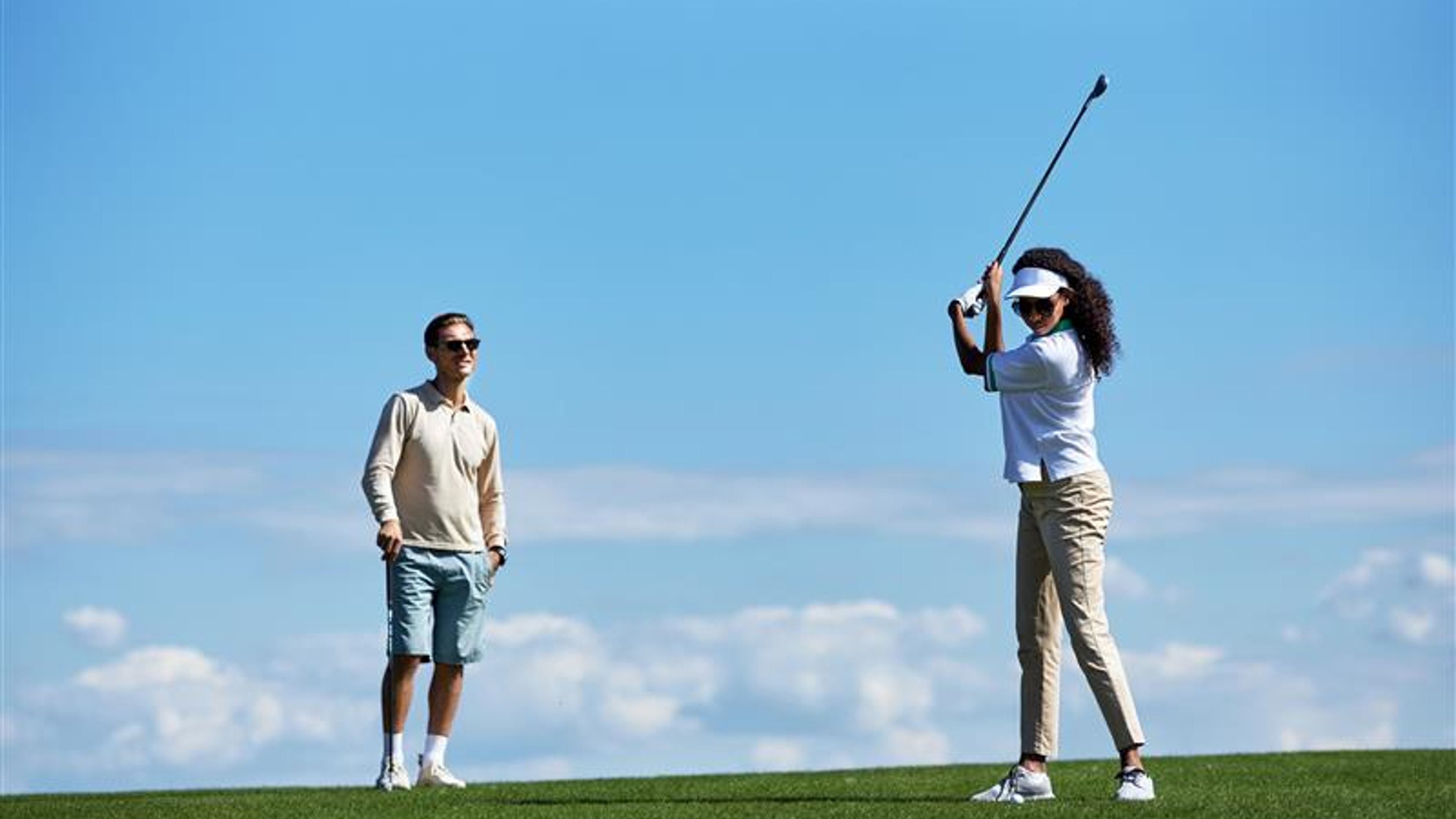 portrait of active sporty couple playing golf against blue sky with woman swinging golf club