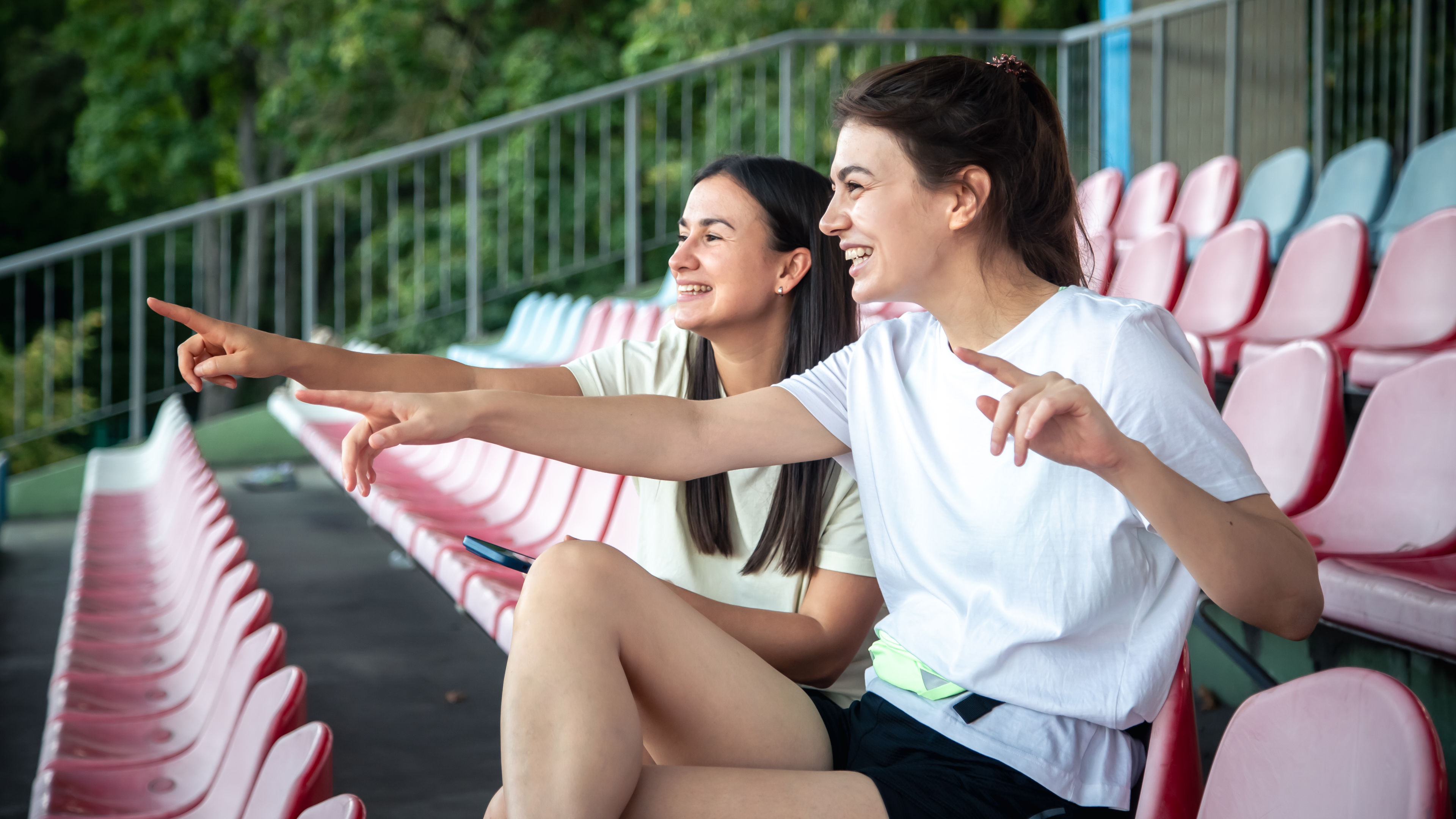 Two young women are sitting in empty stadium seats.
